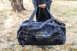 A man holds the Patagonia Black Hole by the duffel straps with the backpack straps attached and hanging to the sides.