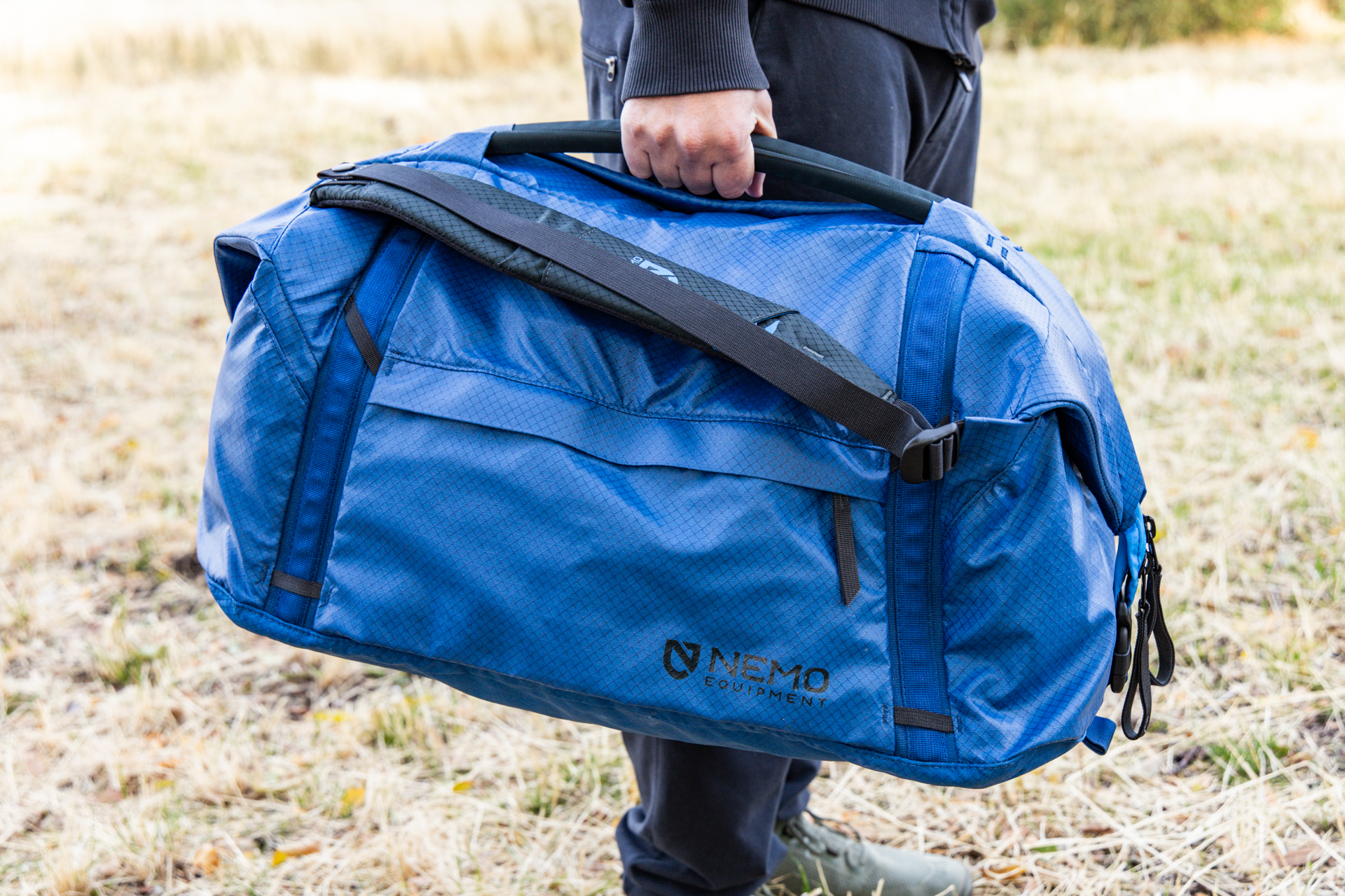 A man carries the Nemo Double Haul in duffel mode using the rigid top handles.