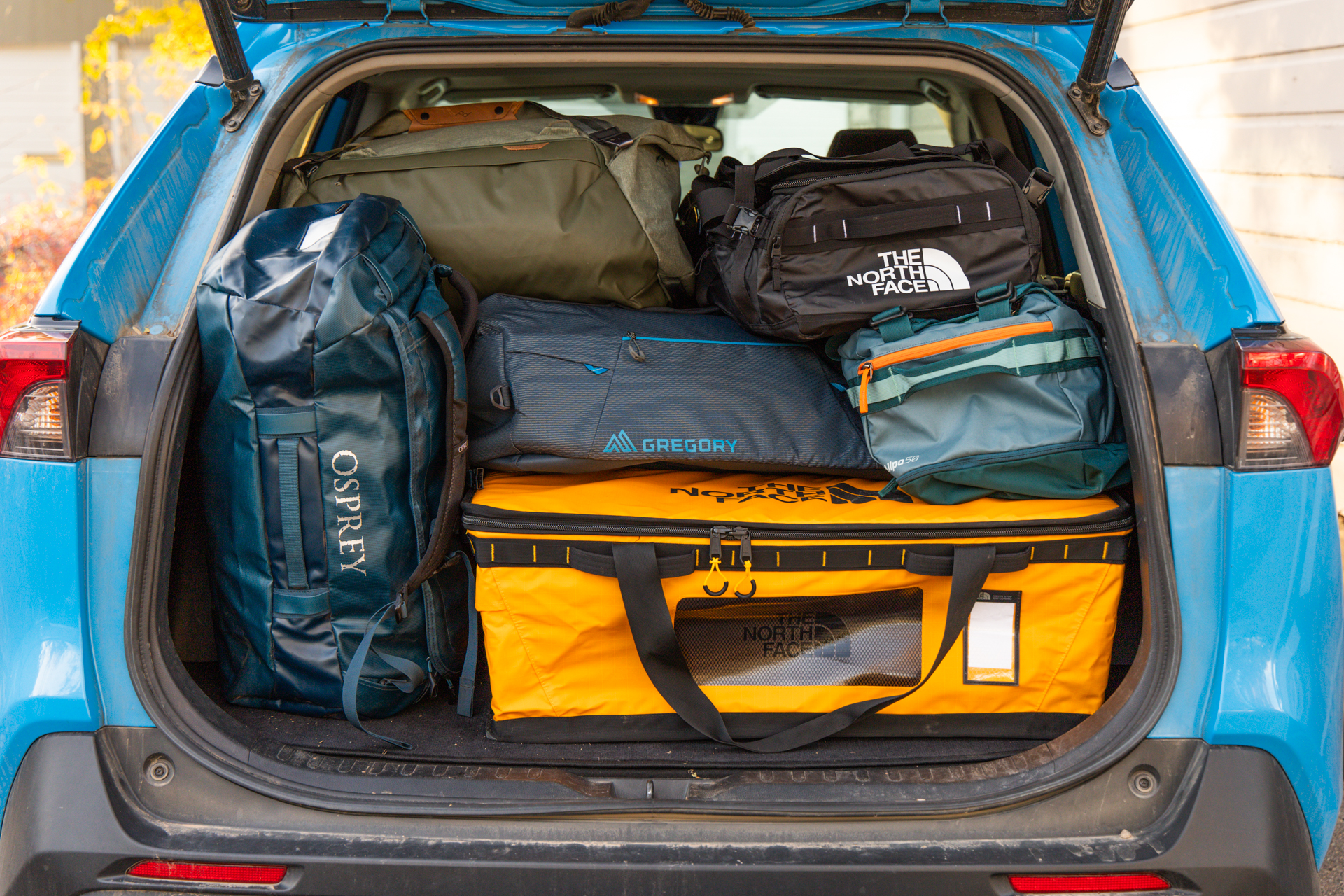 Six different duffels stacked and packed inside the back of an SUV.