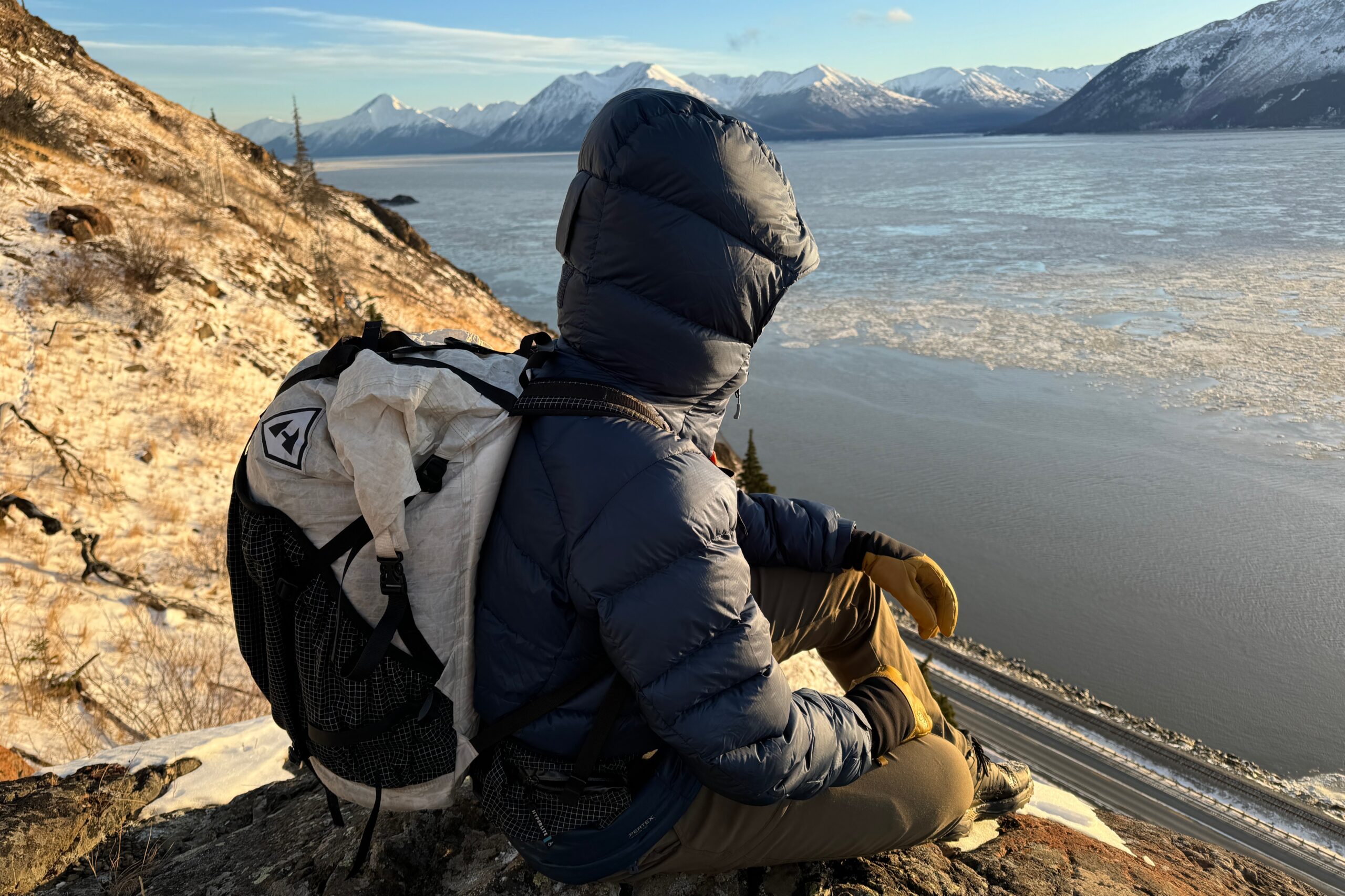 A man sits with his hood up overlooking an ocean view