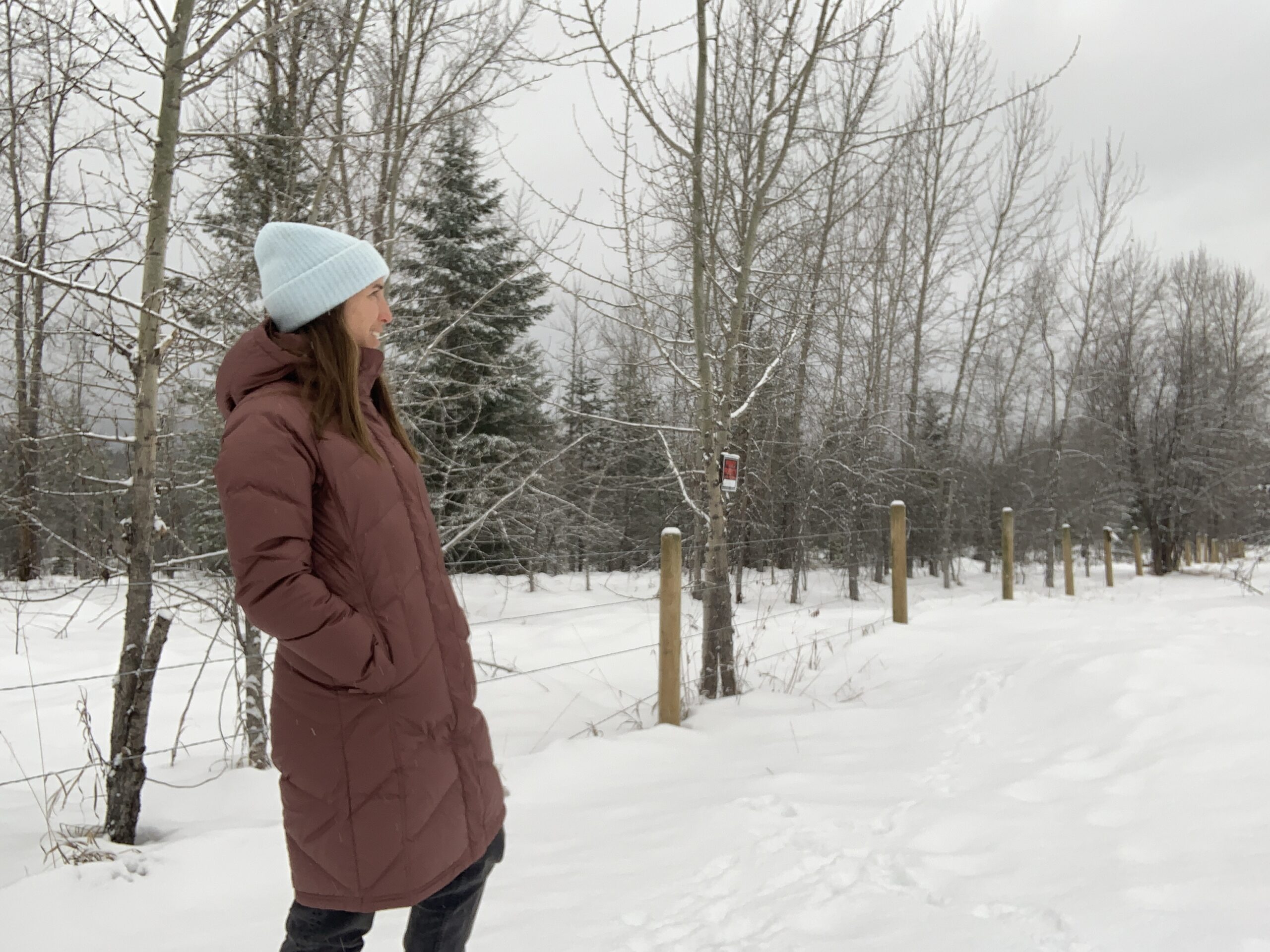 a women walking along a fence on a snowy day with her hands in the pockets of the patagonia down with it parka