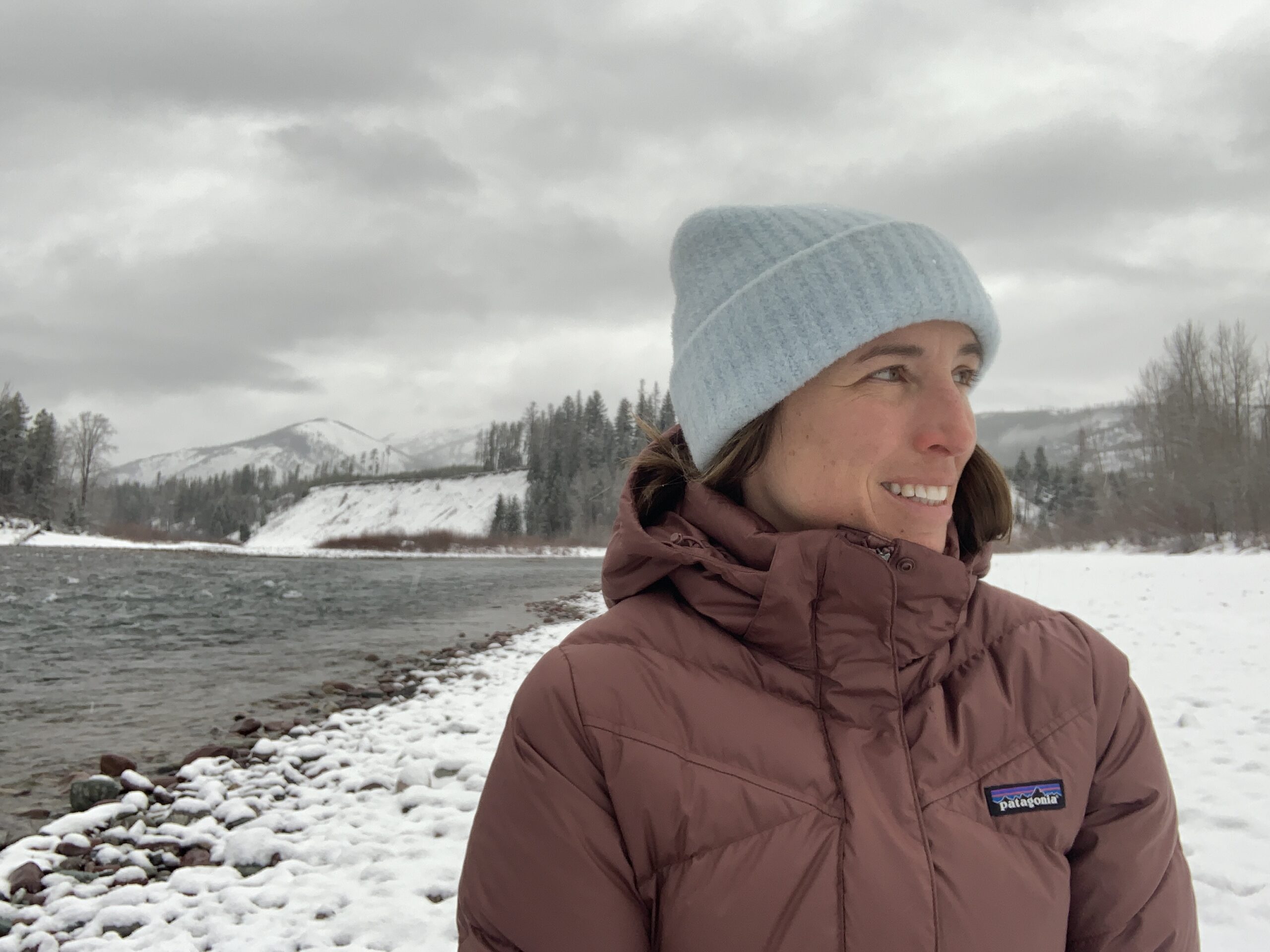 a woman wearing the patagonia down with it women's winter parka while next to a snowy river