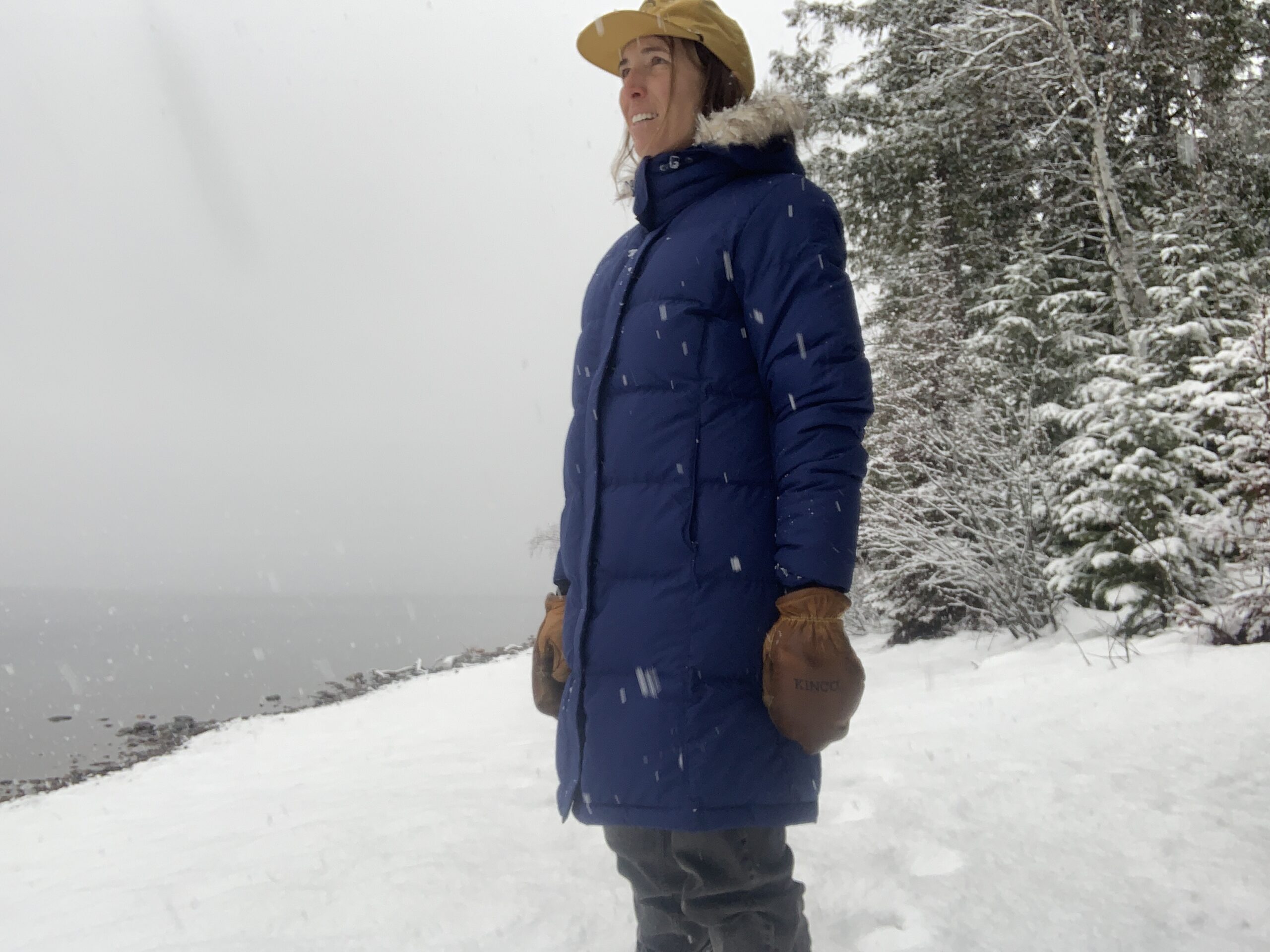 a woman wearing a ll bean down coat standing on the shore of a lake in the snow