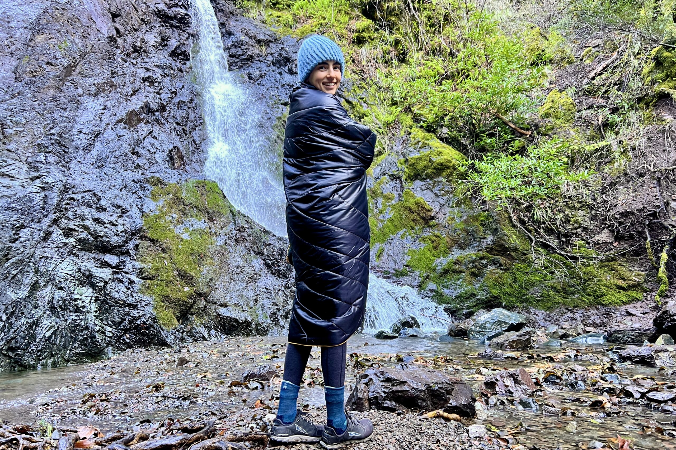 Women standing in front of a waterfall wrapped up in the Rumpl Original Puffy Blanket.