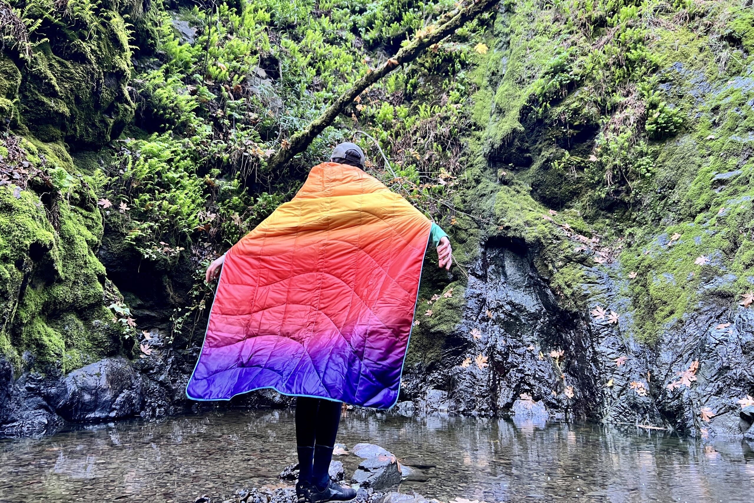 Person standing away from the camera, wearing the Rumpl NanoLoft Puffy as a cape, showing coverage from the back.