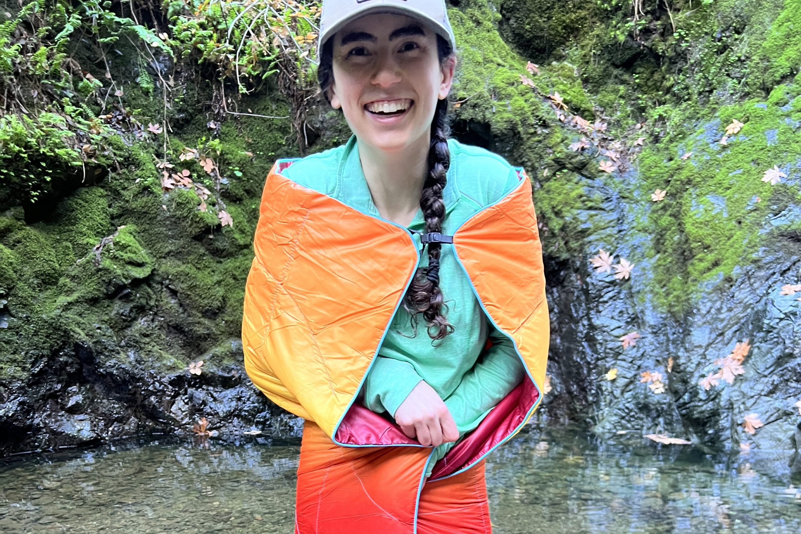 Person wearing the Rumpl NanoLoft Puffy Blanket in cape mode and wrapping the blanket around her body to show its minimal coverage.