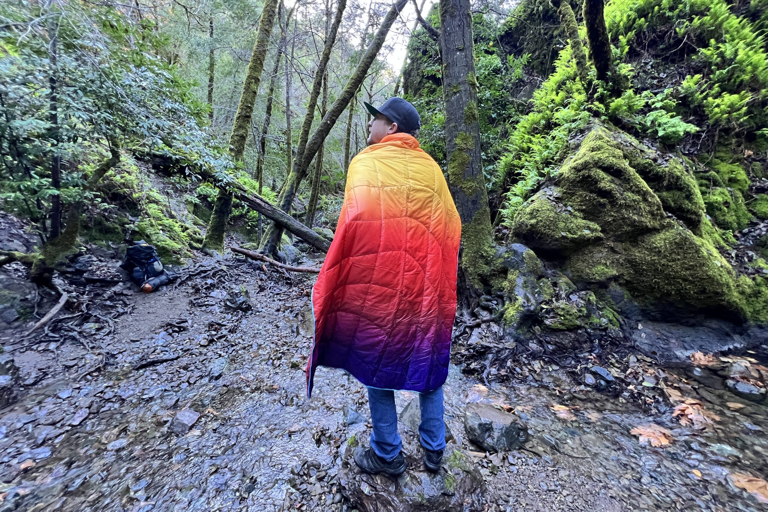 Person standing in the forest wearing the Rumpl NanoLoft Puffy Blanket.