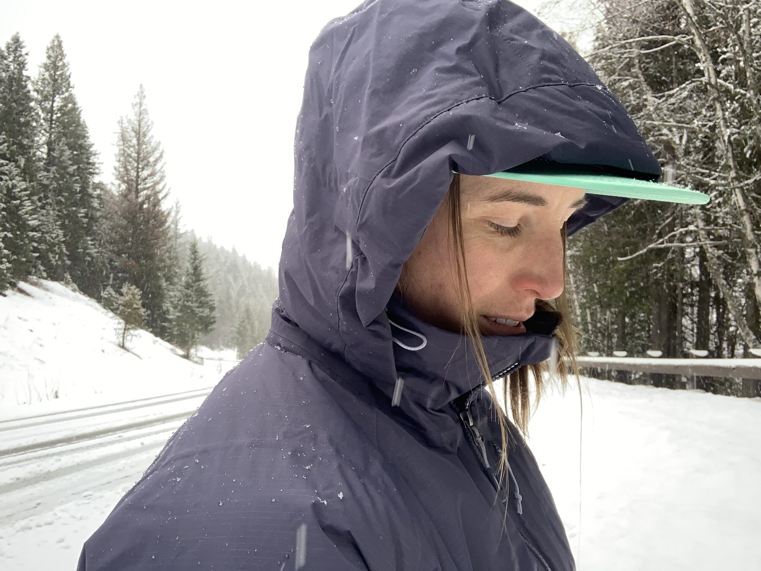 a close up of a women wearing the REI stormhenge hybrid 850 down parka showing how the shell and hood repel snow and water