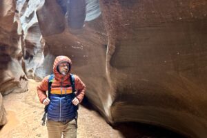 A man in a puffy jacket smiles as he walks through a desert canyon.