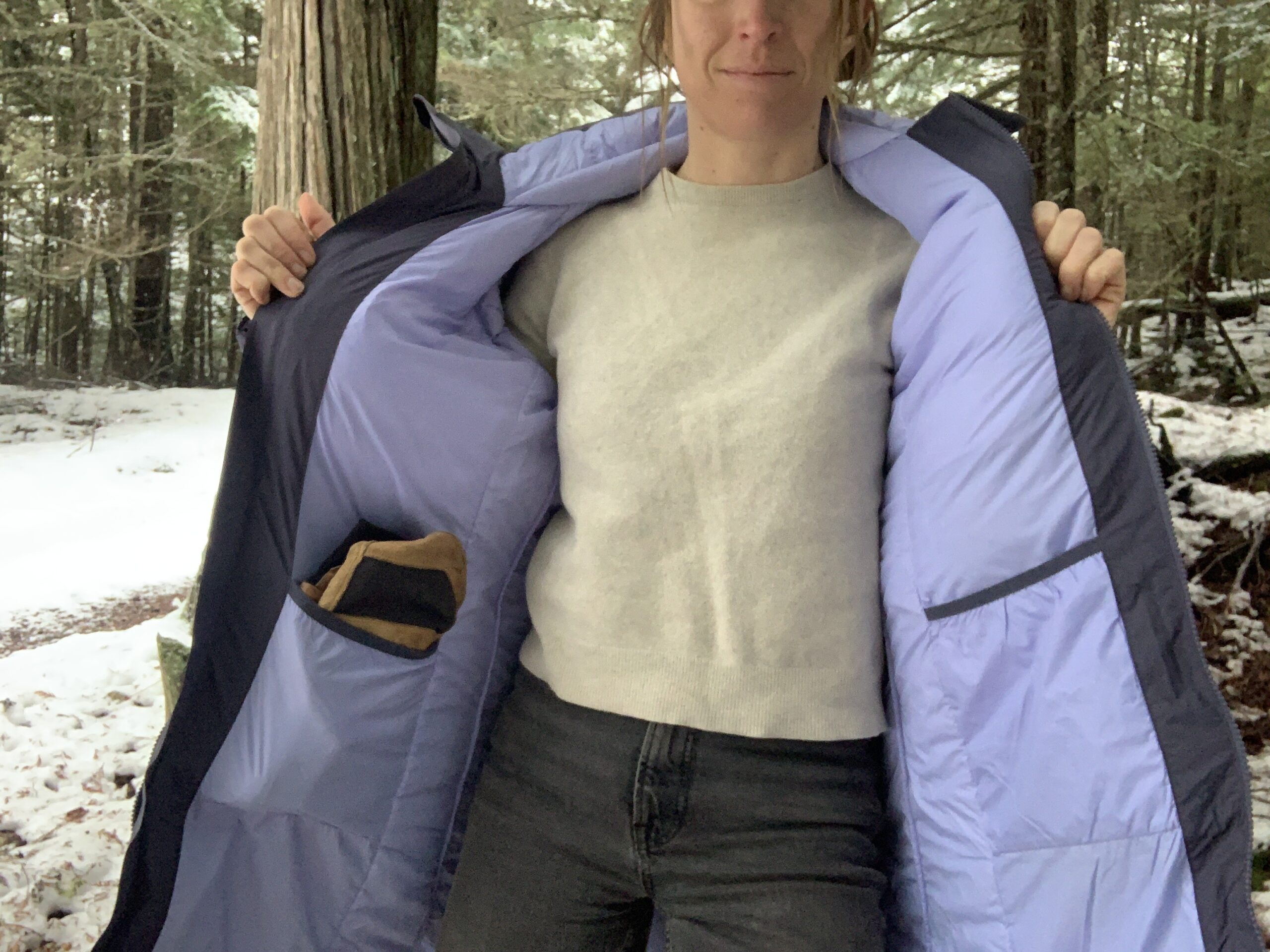 a woman shows the inside of the REI stormhenge 850 hybrid parka to show two large drop pockets