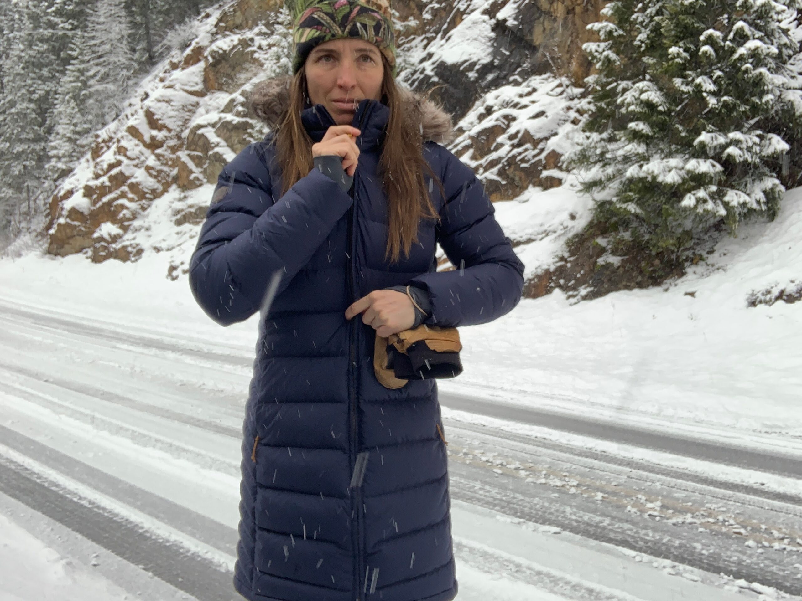 a woman zipping up the rab deep cover parka on the side of a snowy road