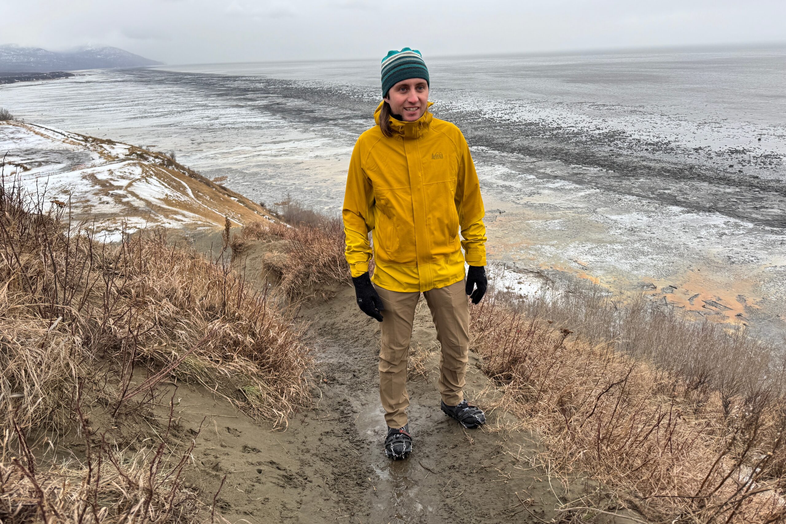 A man hikes above a muddy and icy coastline.