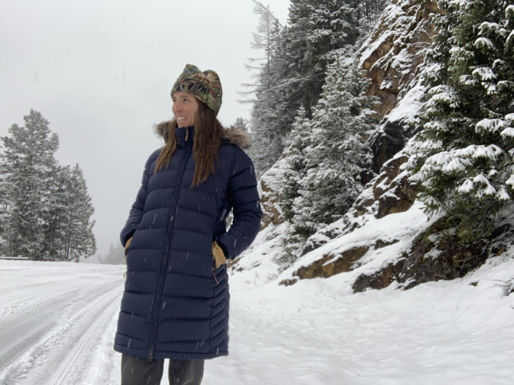 a woman standing on the side of a snow covered road wearing the rab deep cover parka