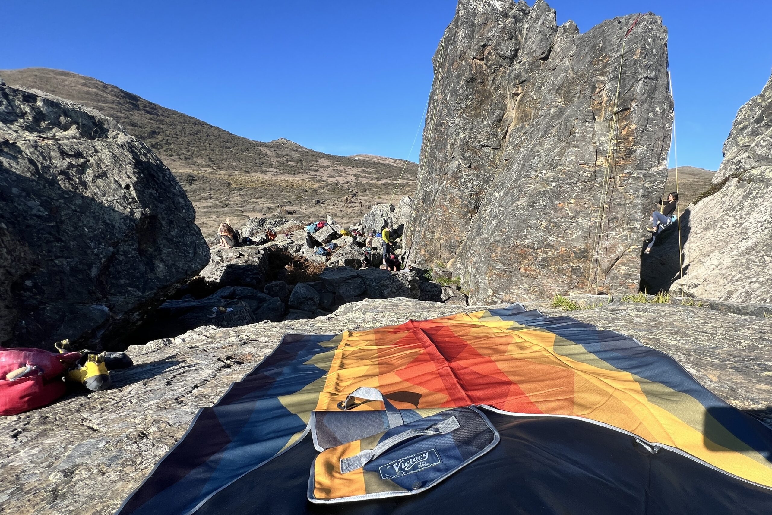 The Nemo Victory Patio Blanket is spread out on a rock overlooking some rock climbers.