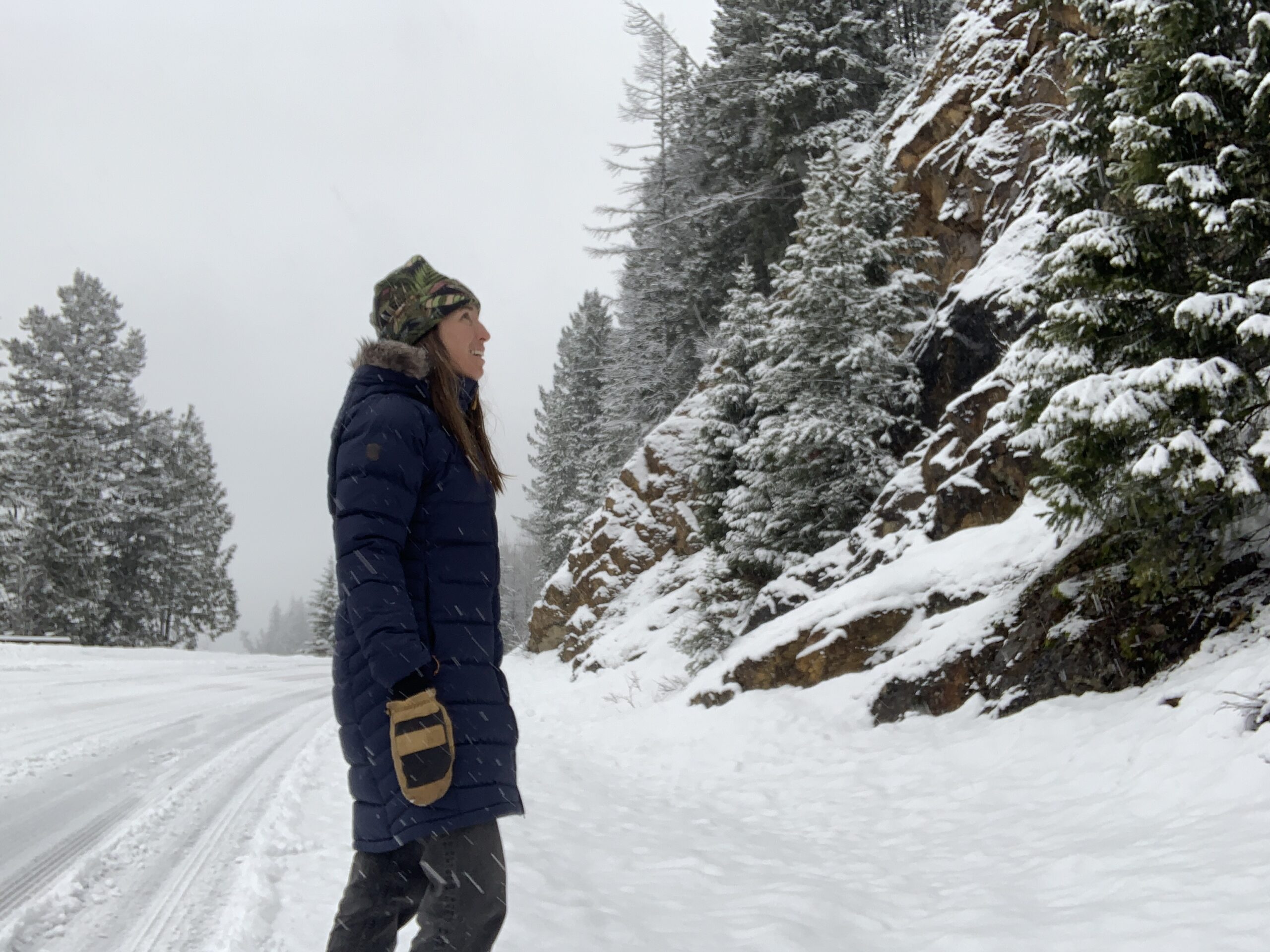 a woman looks at the rocks along a snow covered road while wearing the rab deep cover parka