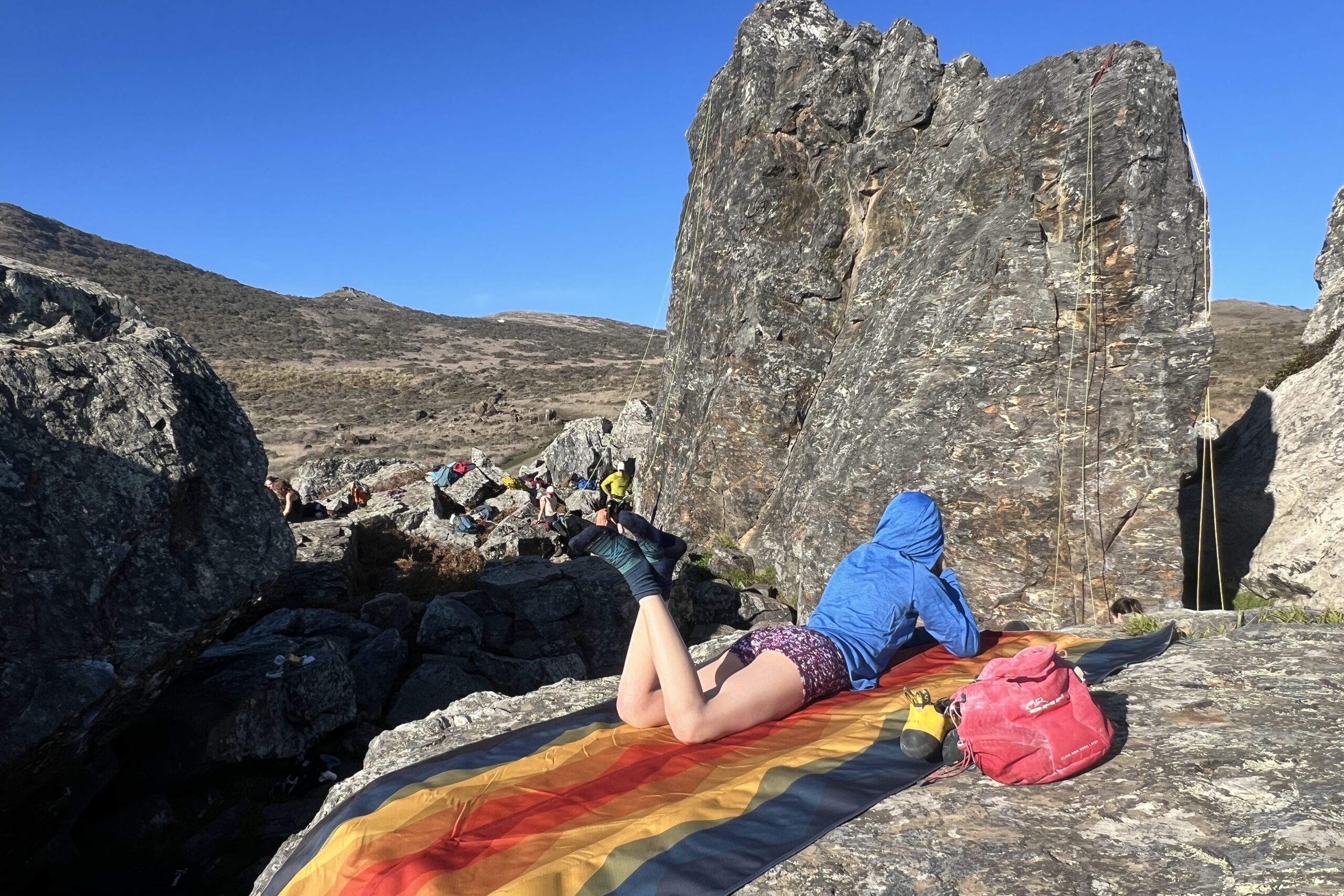 Woman laying out on the Nemo Victory Patio Blanket in front of a rock climbing scene.