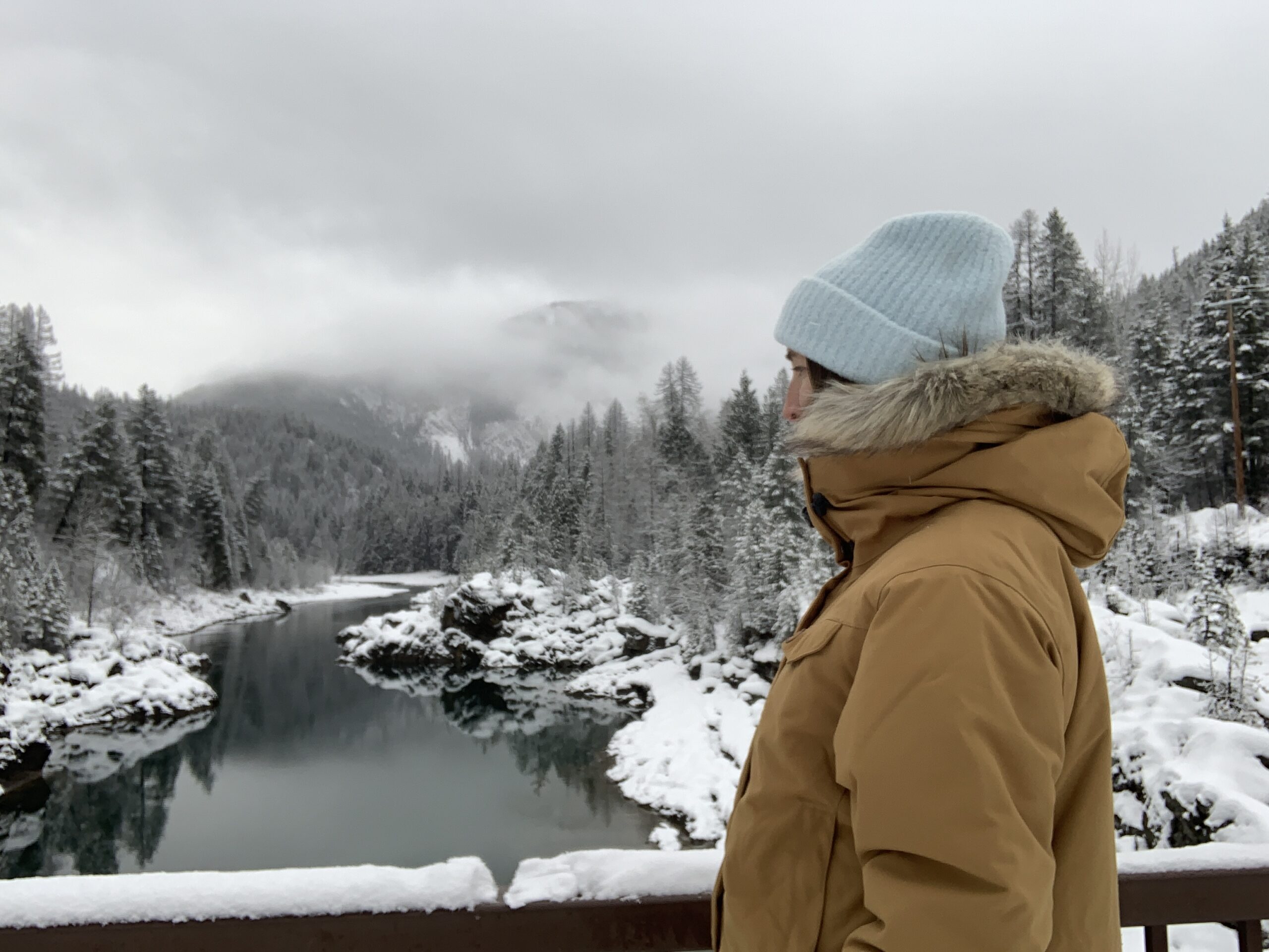 a woman standing on a bridge over a snowy glacial river wearing the fjallraven nuuk