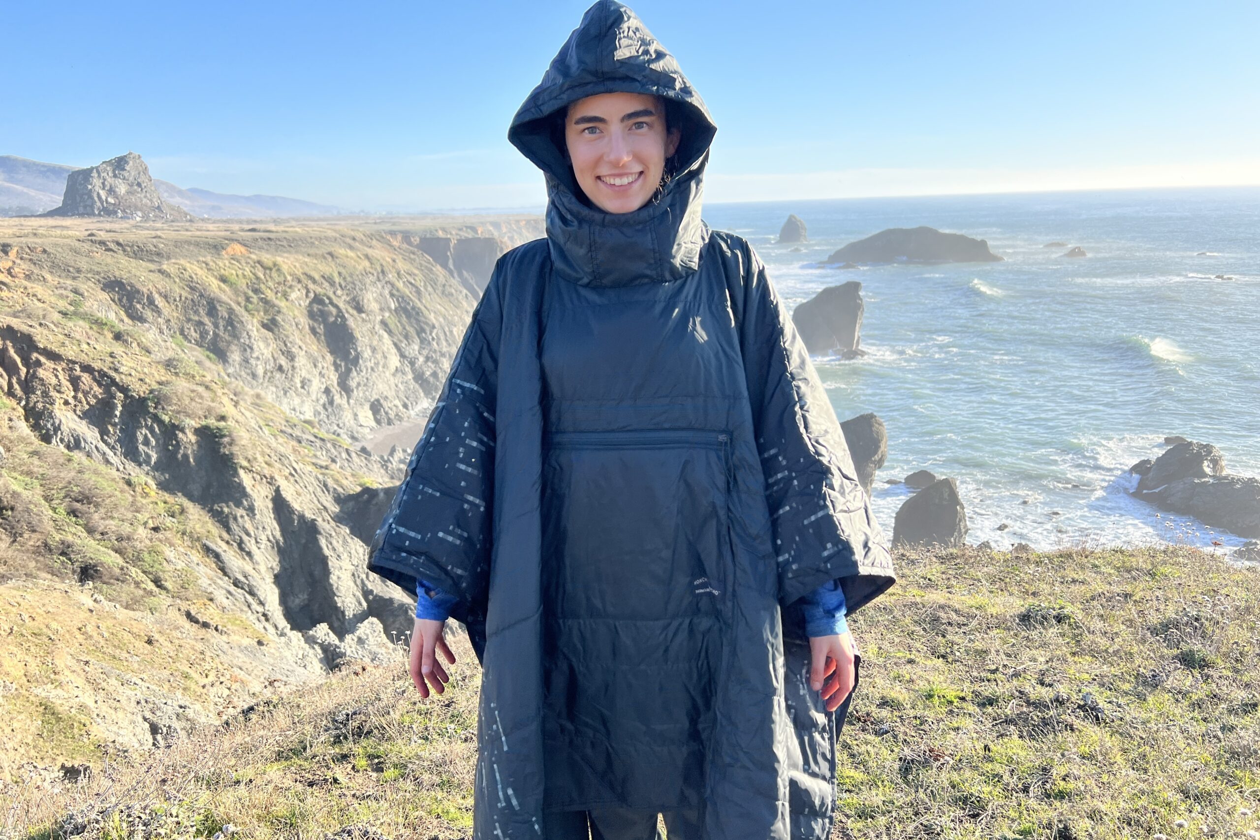 Woman wearing the Therm-a-Rest Honcho Poncho on a coastal bluff.