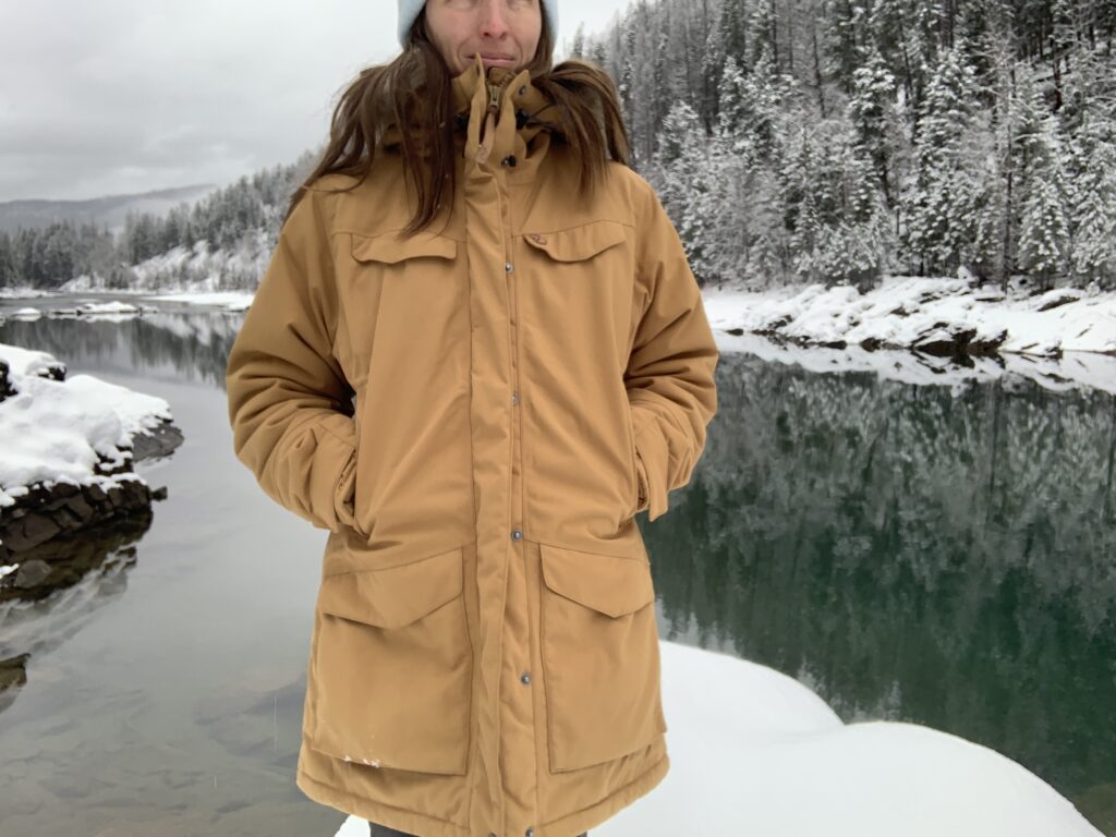 a woman wearing the fjallraven nuuk while standing in the front of a glacial river