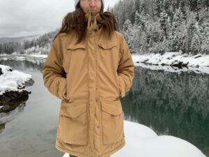 a woman wearing the fjallraven nuuk while standing in the front of a glacial river