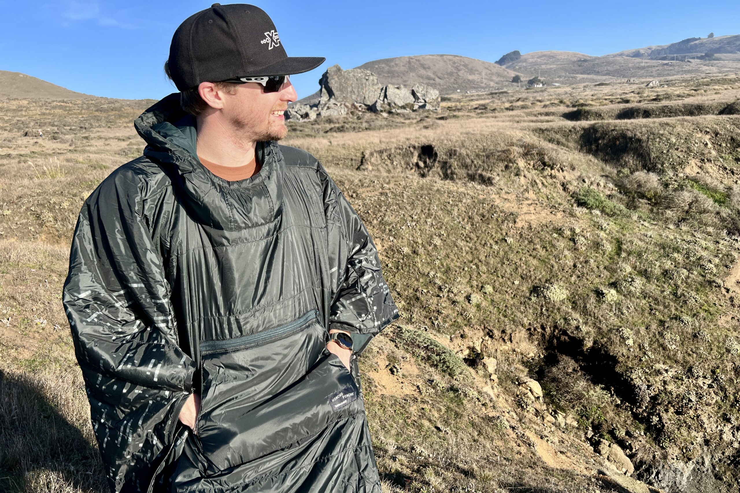 Man wearing the Therm-a-Rest Honcho Poncho and using the 2 included hand pockets for warmth.