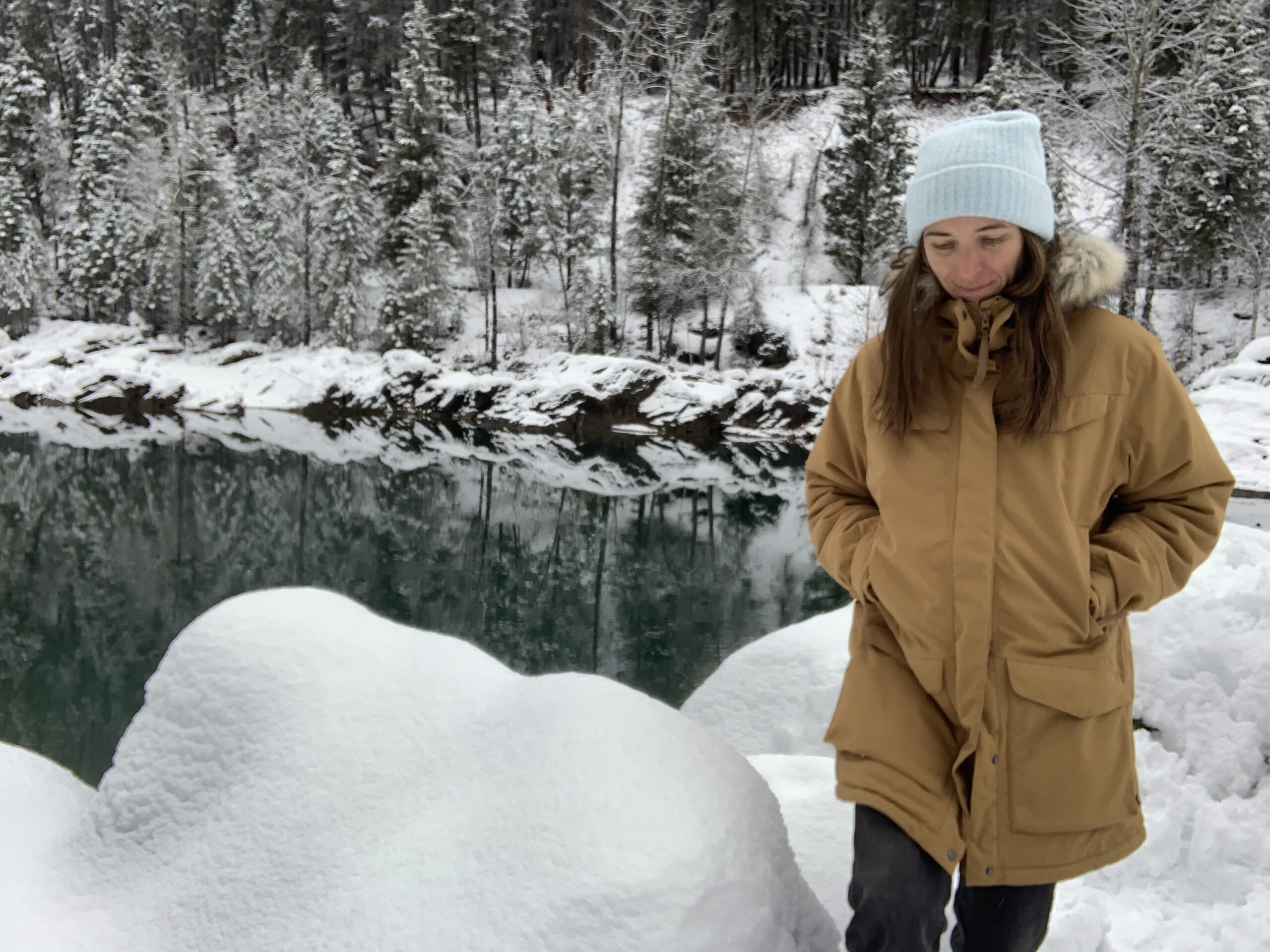 a woman walking through snow covered boulders next to a glacial river while wearing the fjallraven nuuj