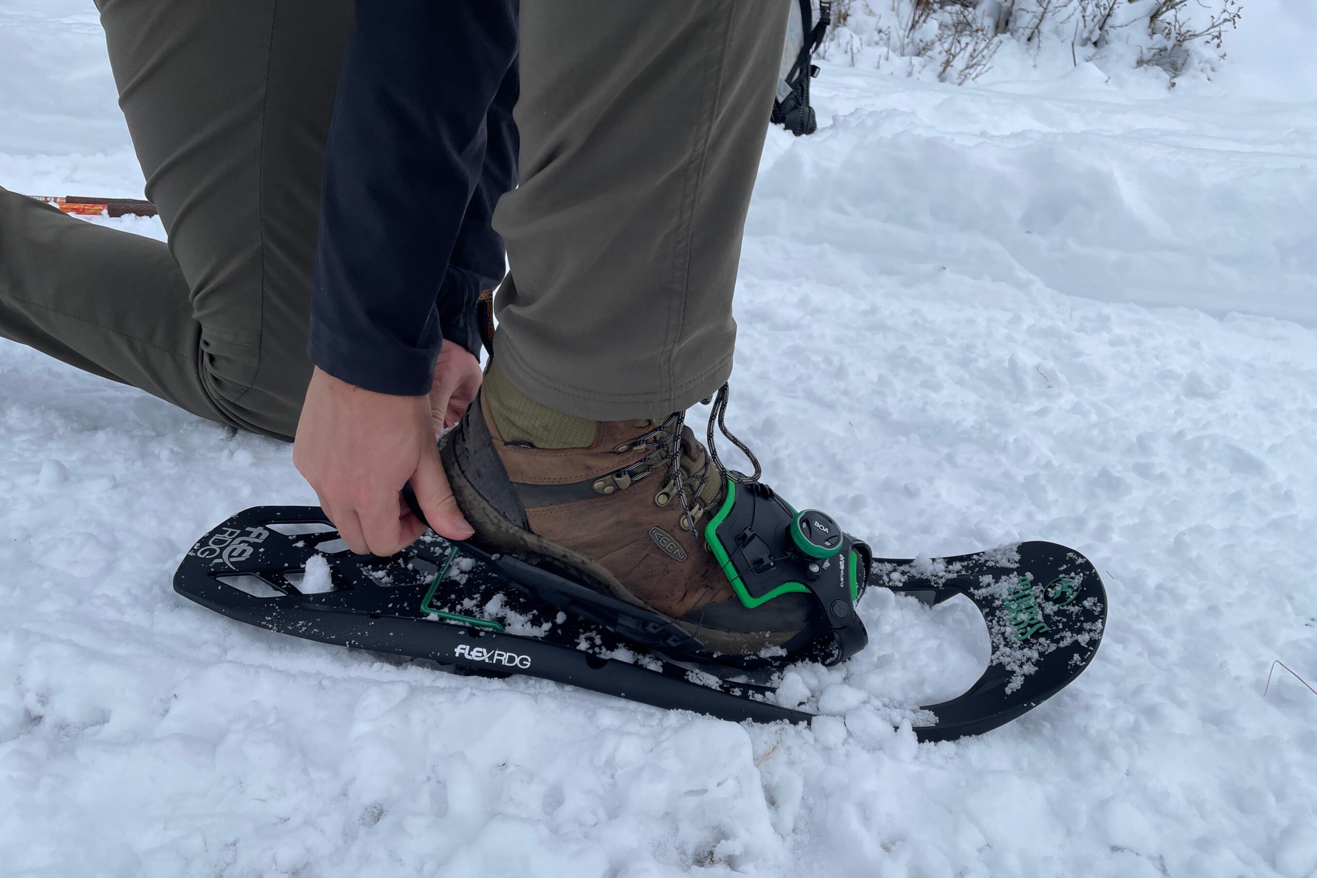 a hiker reaching to the heel of their snowshoe to attach their boot to the shoes