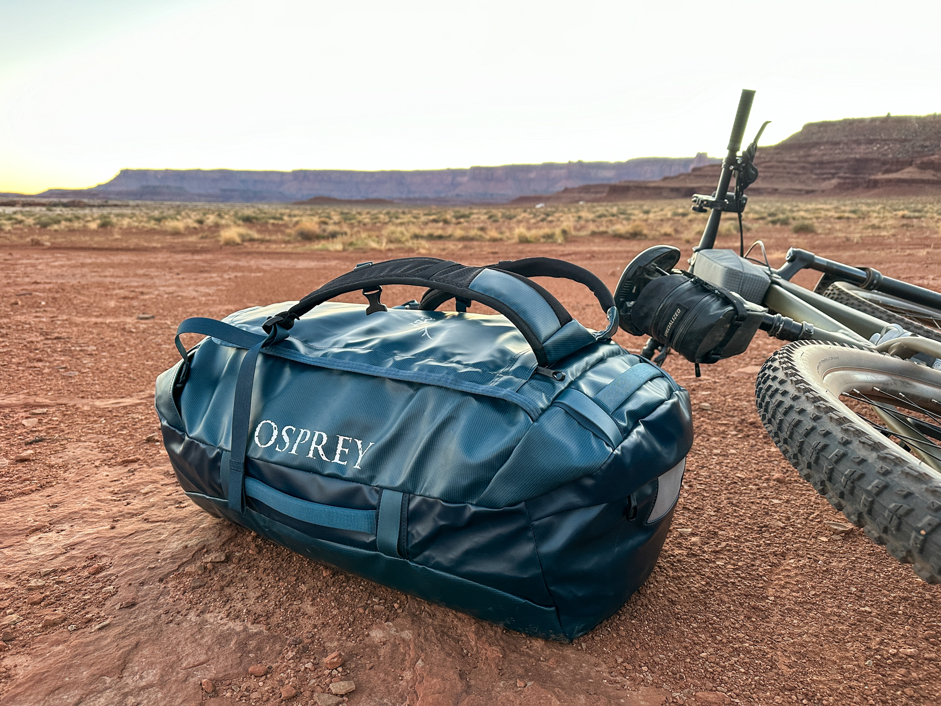 The Osprey Transporter duffel packed and sitting next to a bike in the desert.