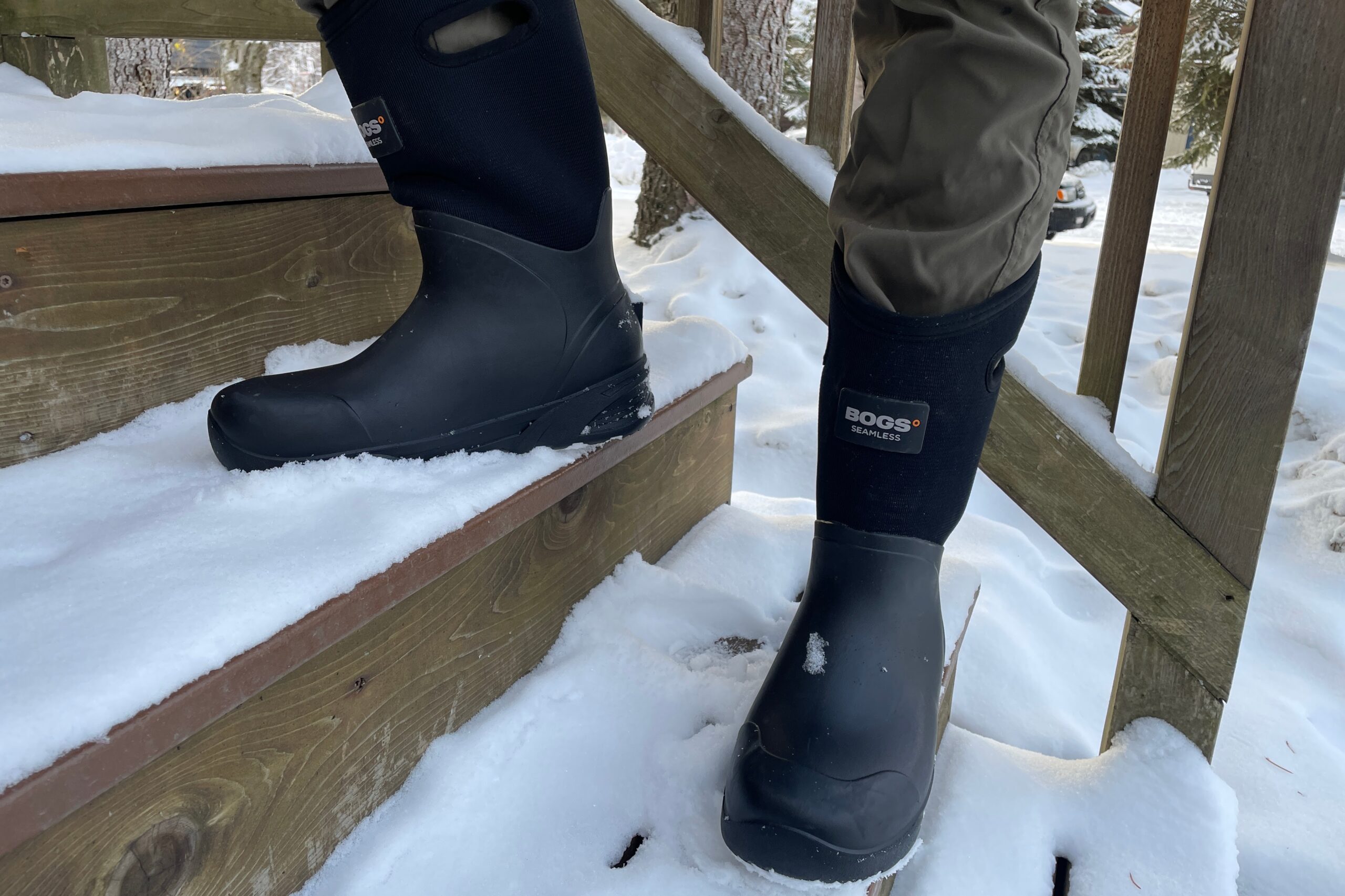 A man stands on snowy steps showing the logo of a pair of boots.