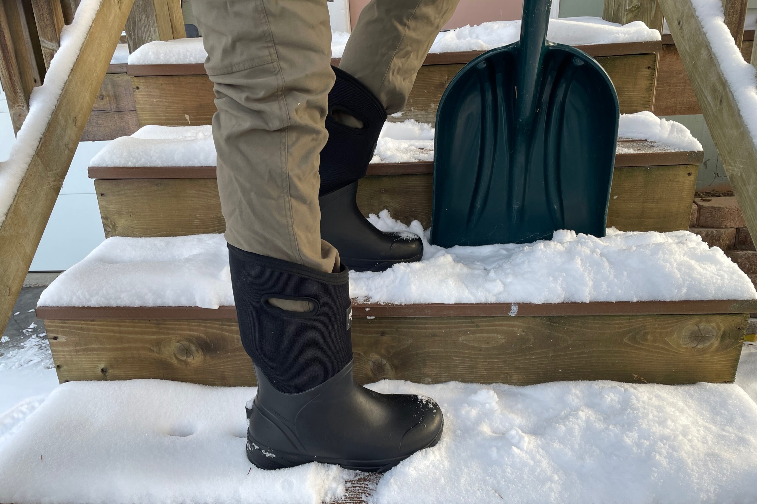 A pair of boots on snowy steps next to a shovel.