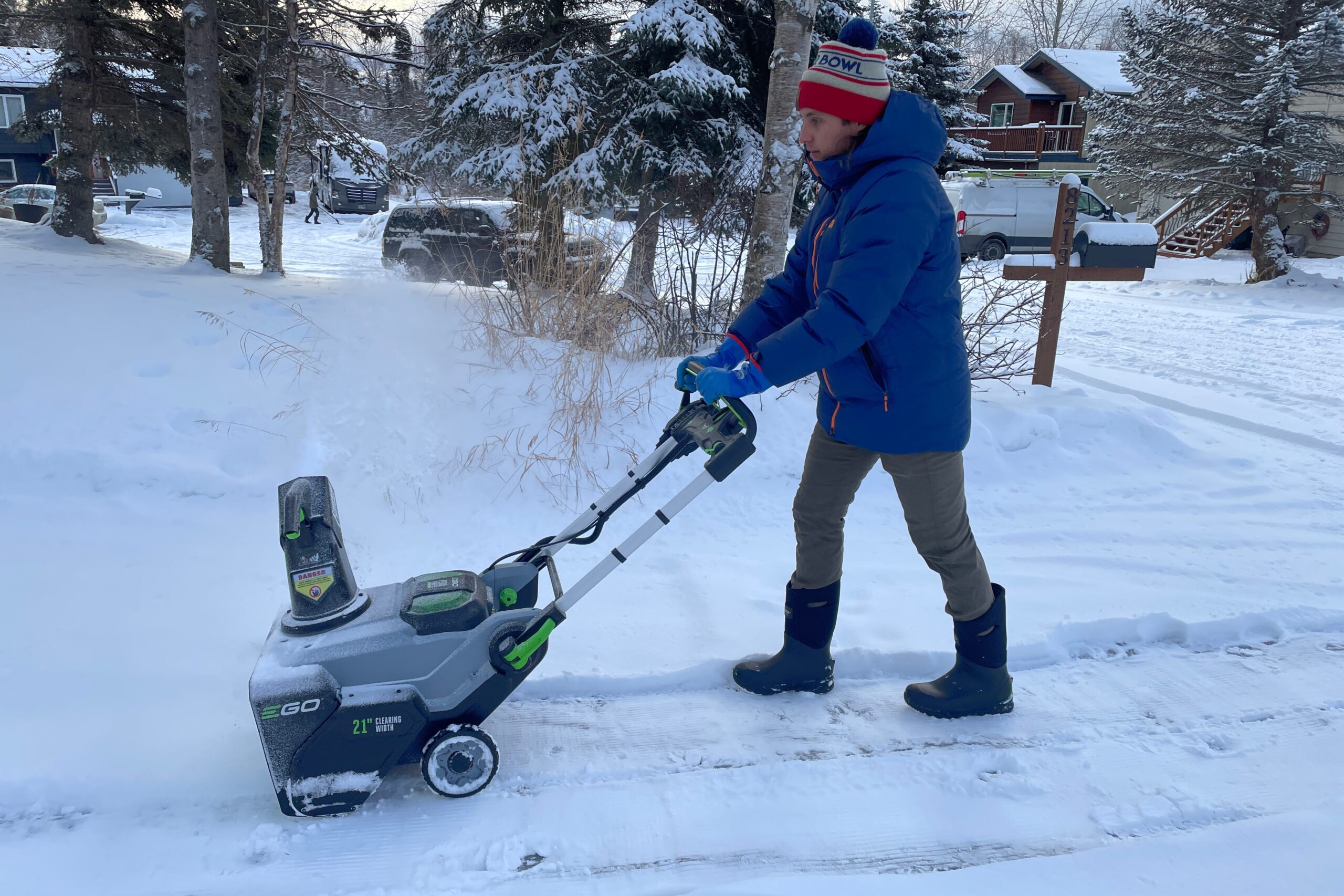 A man snowblows a driveway wearing winter gear.