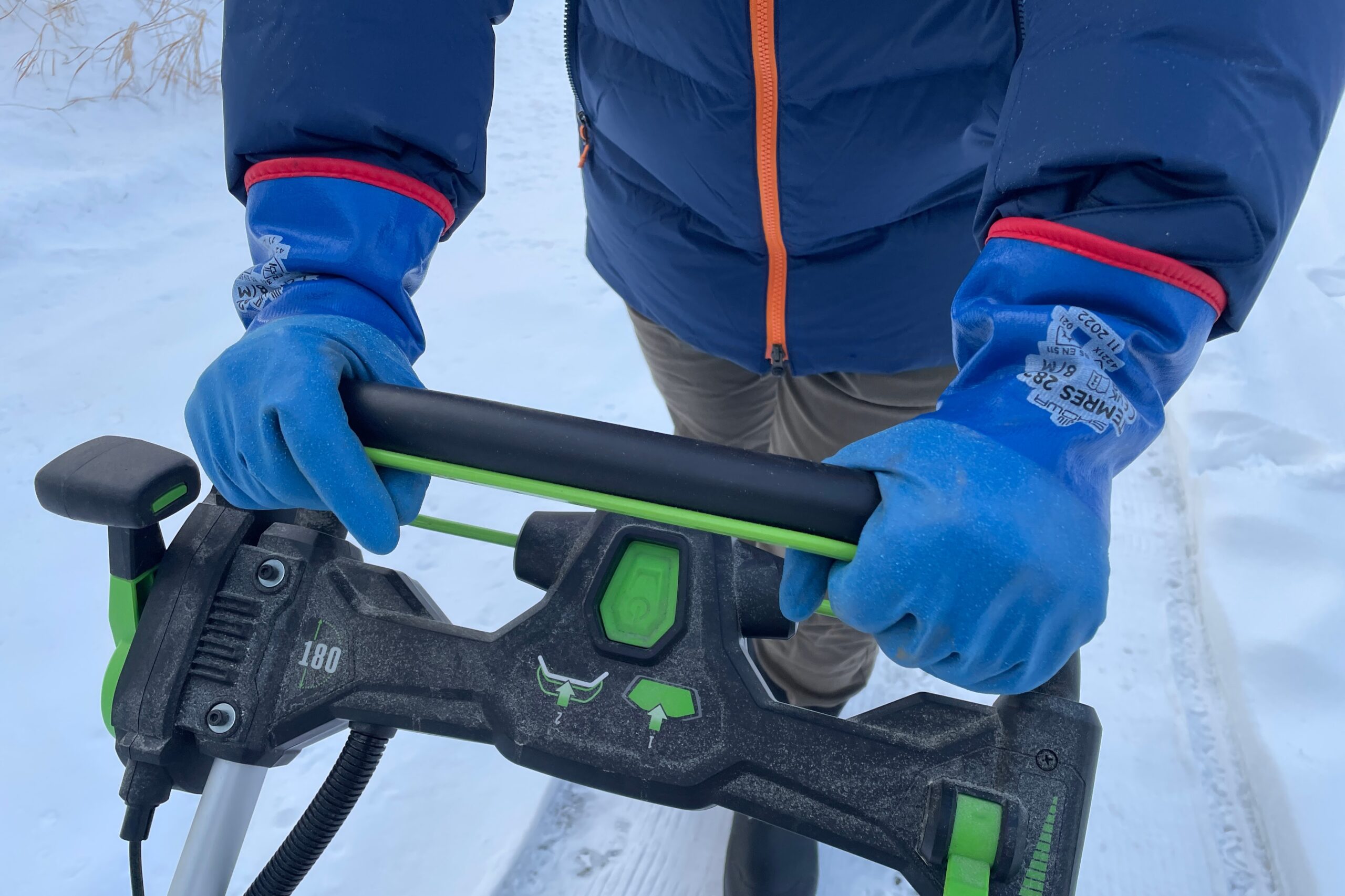 A closeup of gloves holding onto the grip of a snowblower.