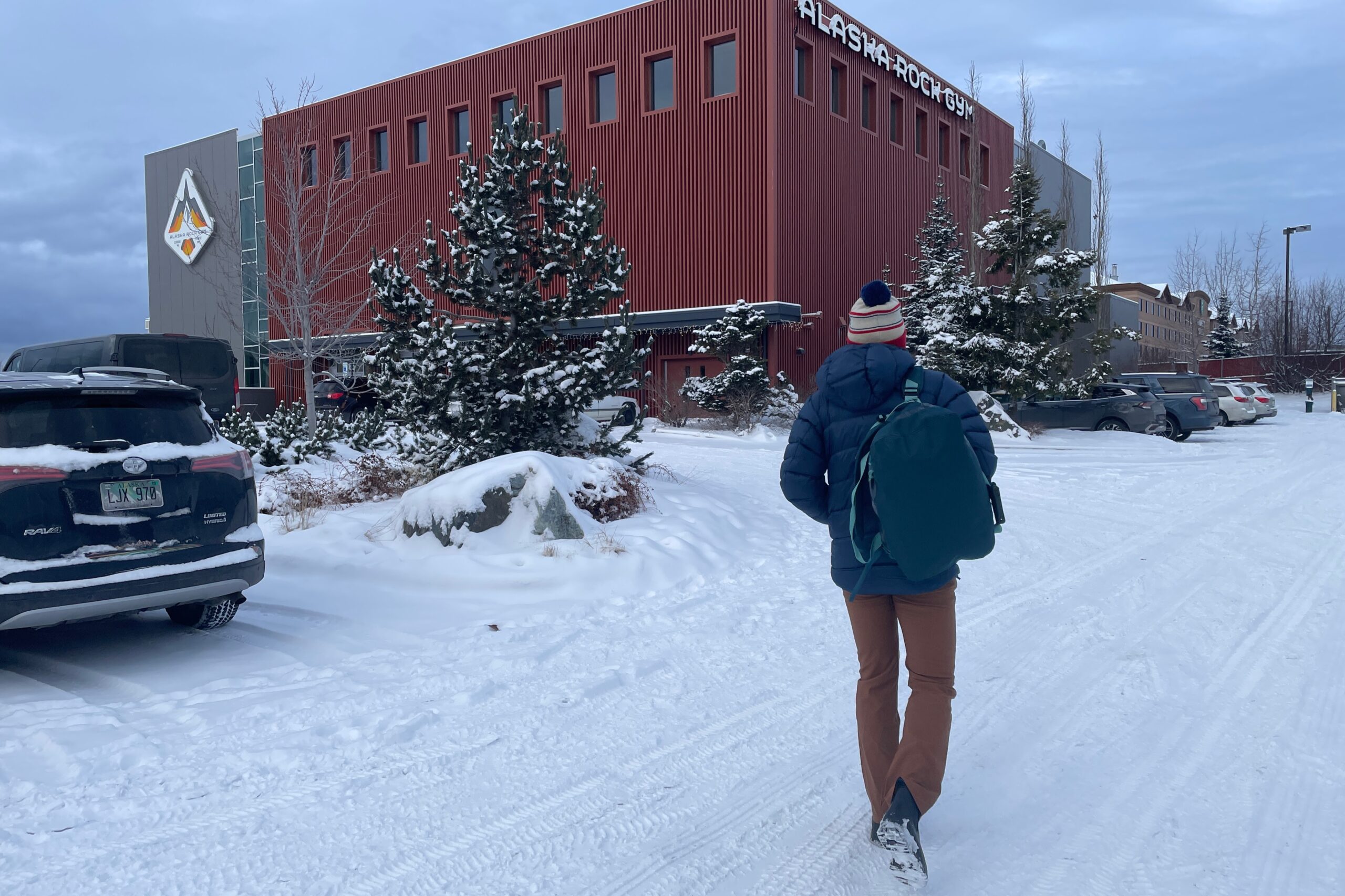 A man walks to a climbing gym across a snowy parking lot.