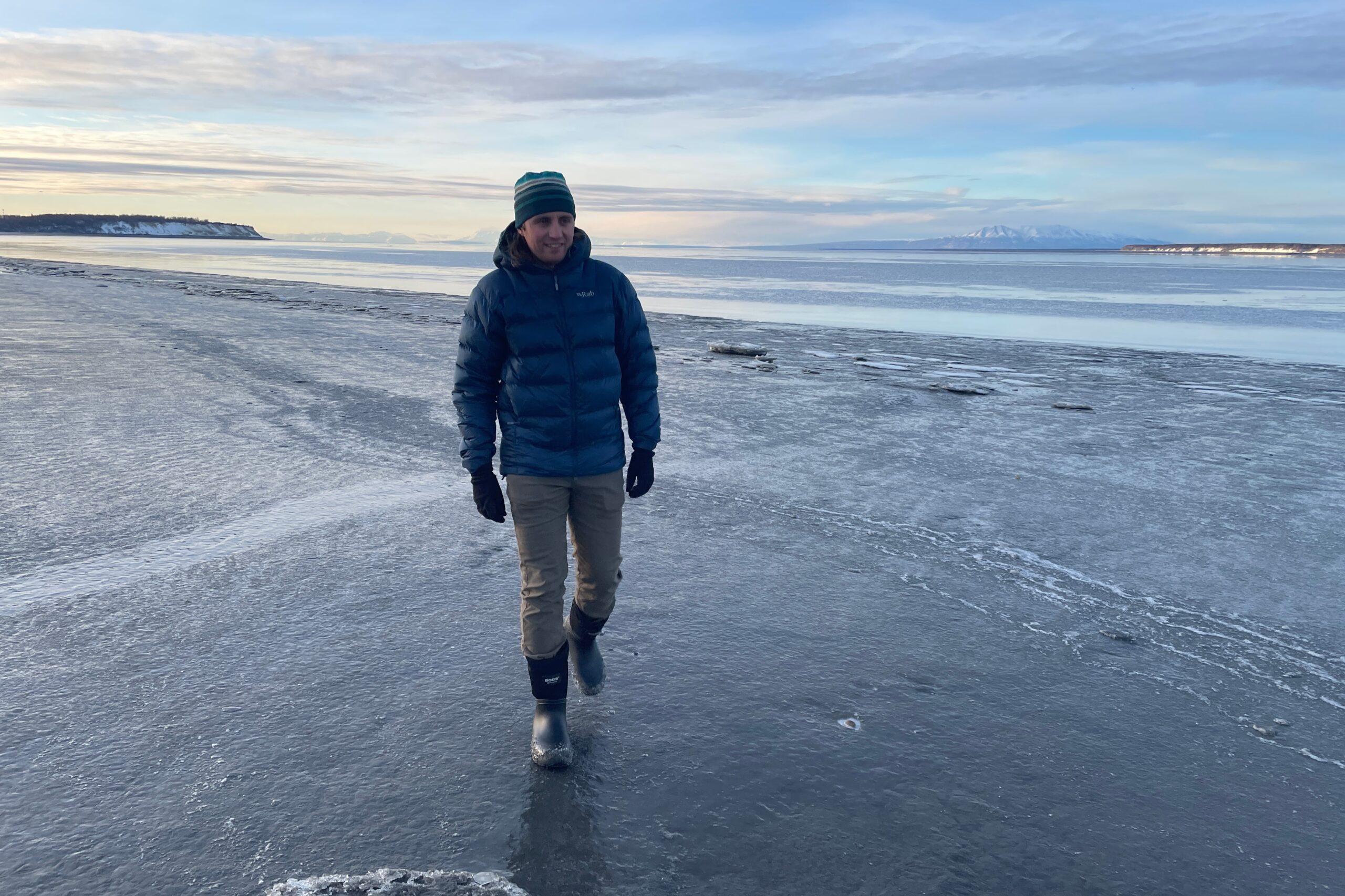 A man walks along the muddy shores of the ocean.