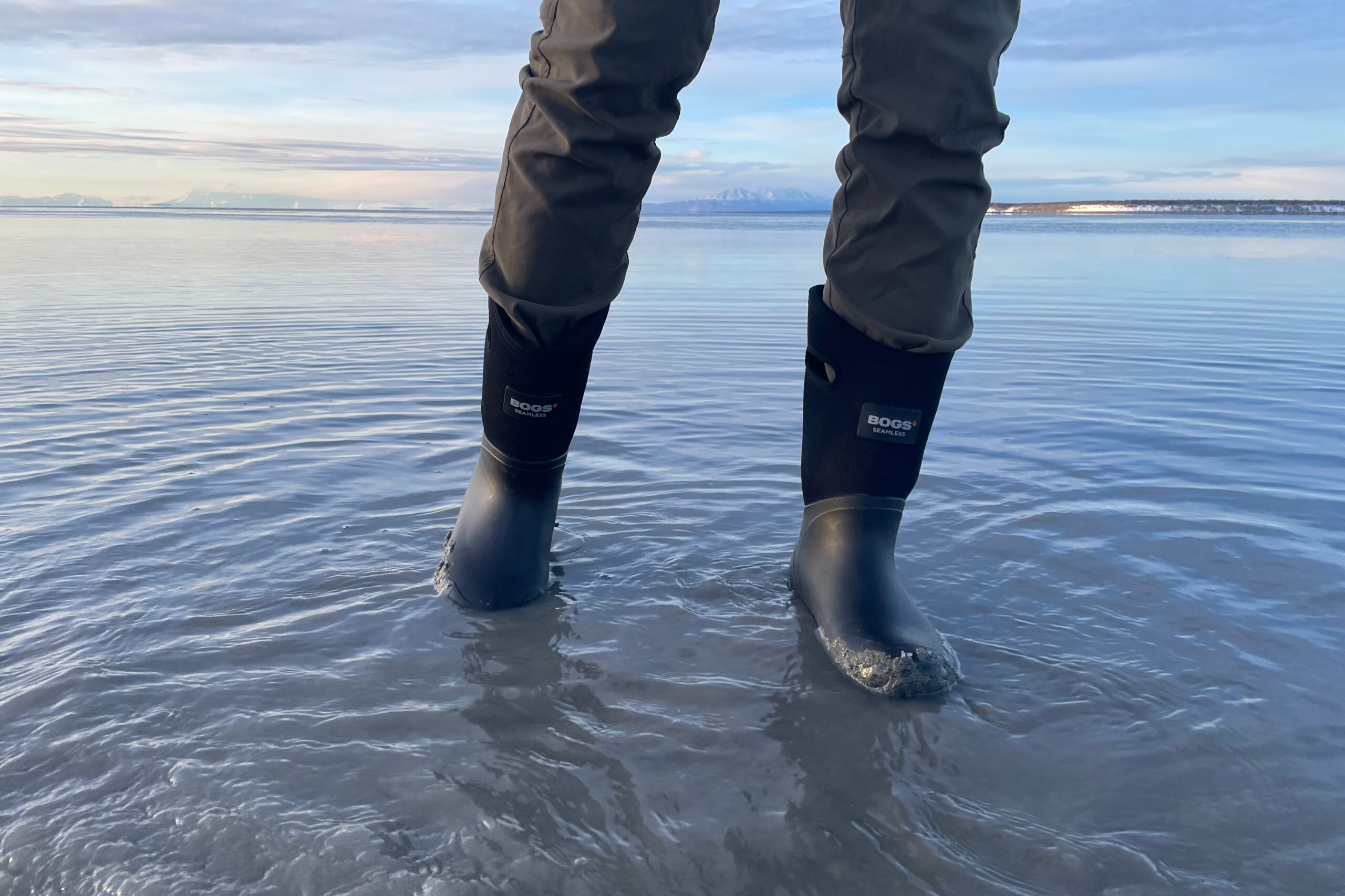 A man stands in rubber boots in muddy water.