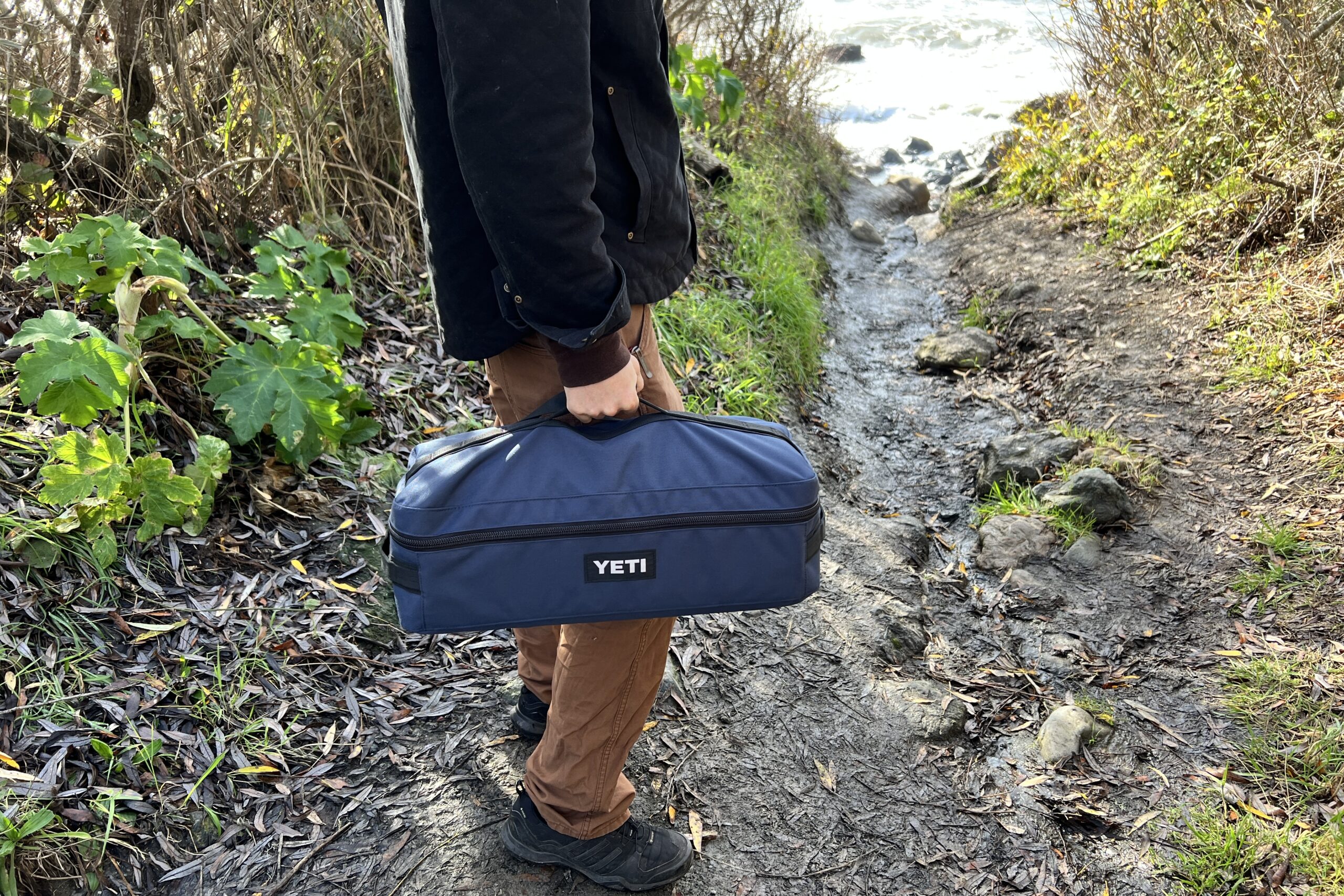 Man holding the handle of the Yeti Lowlands Blanket carry case on a hike to the beach.