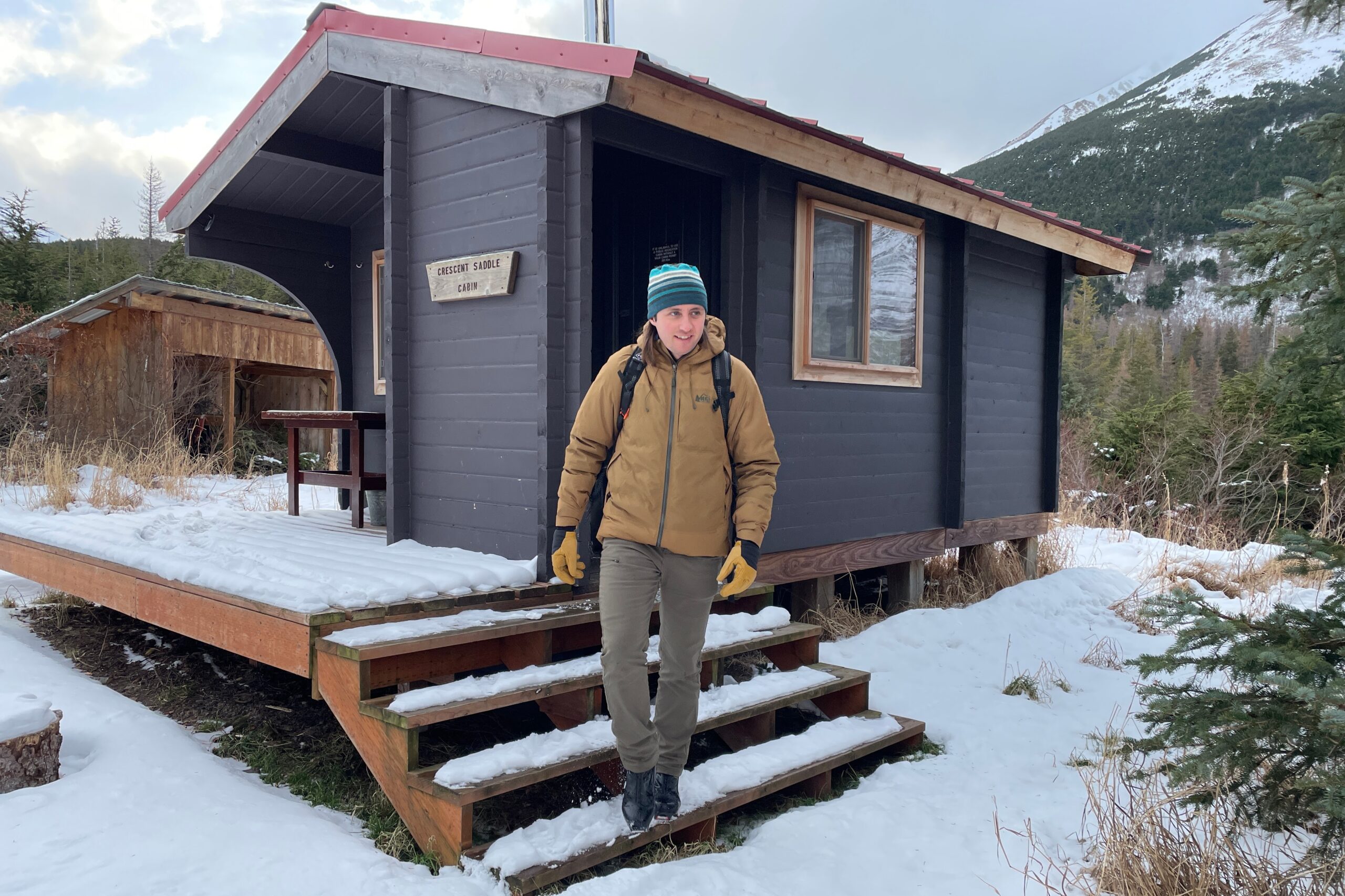 A man walks out of a cabin in the woods.