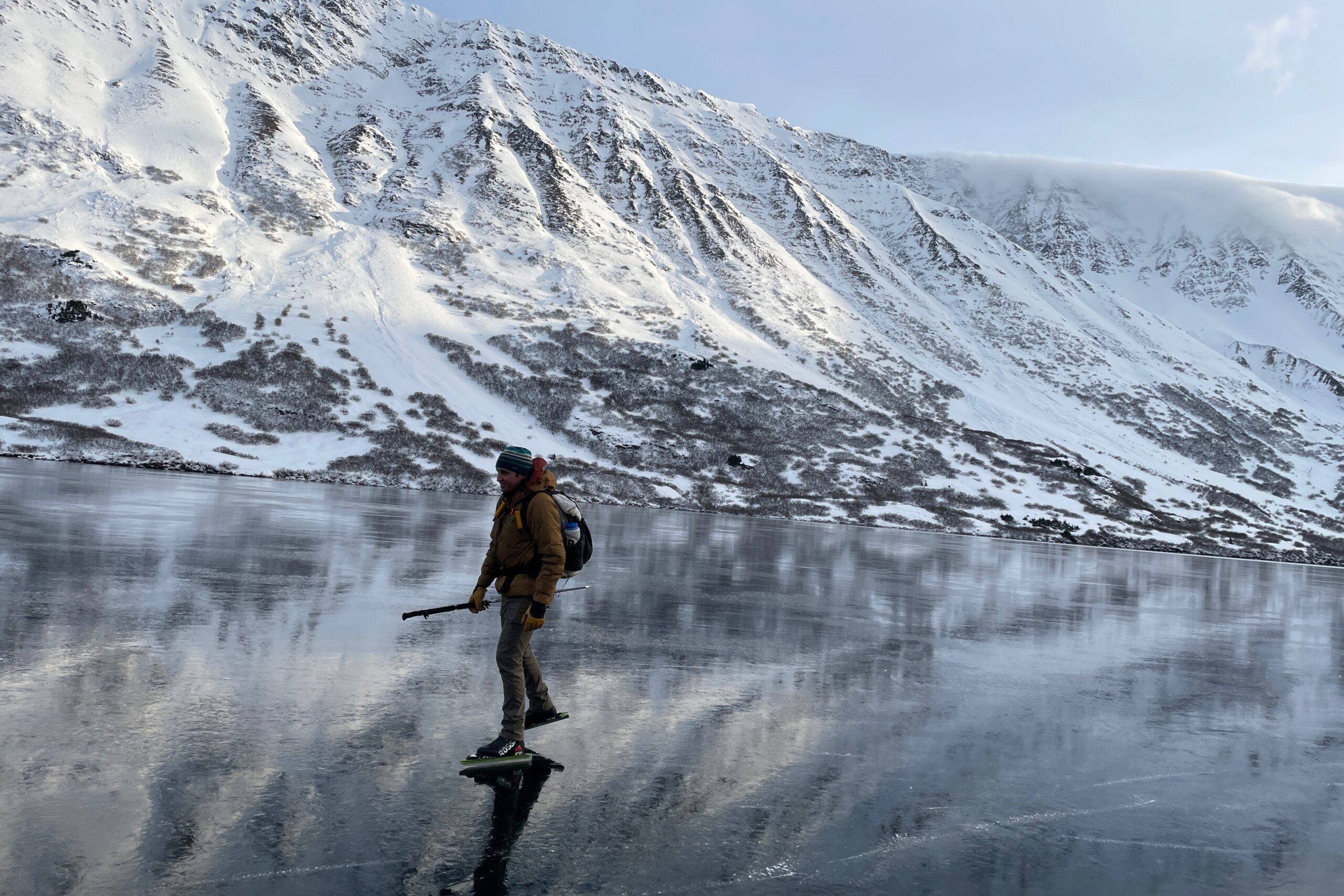 A man ice skates across a mountain lake.