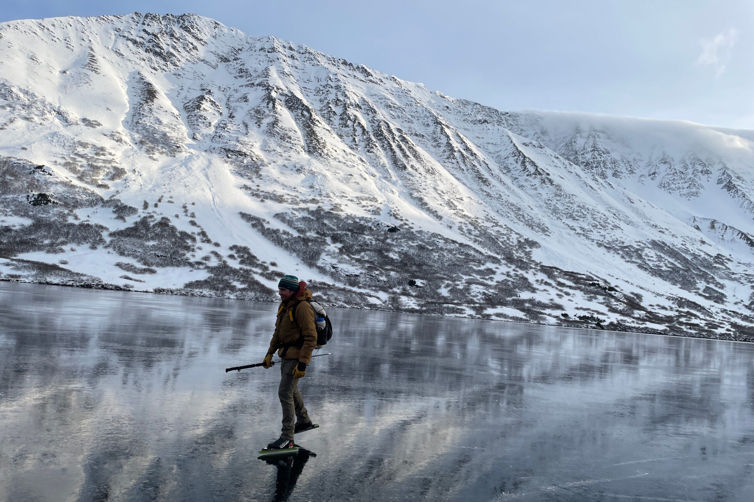 A man ice skates across a mountain lake.