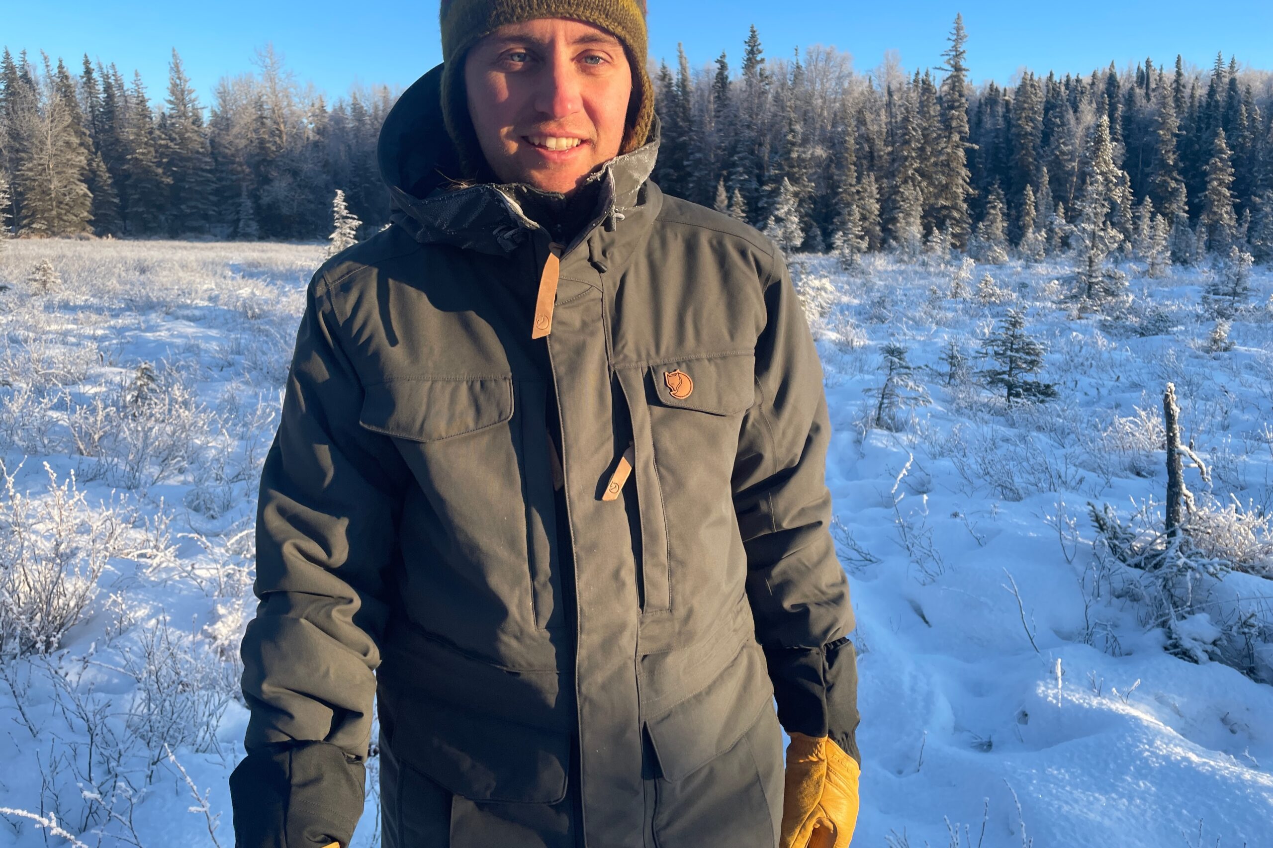 A man walks through a sunny meadow covered in snow.