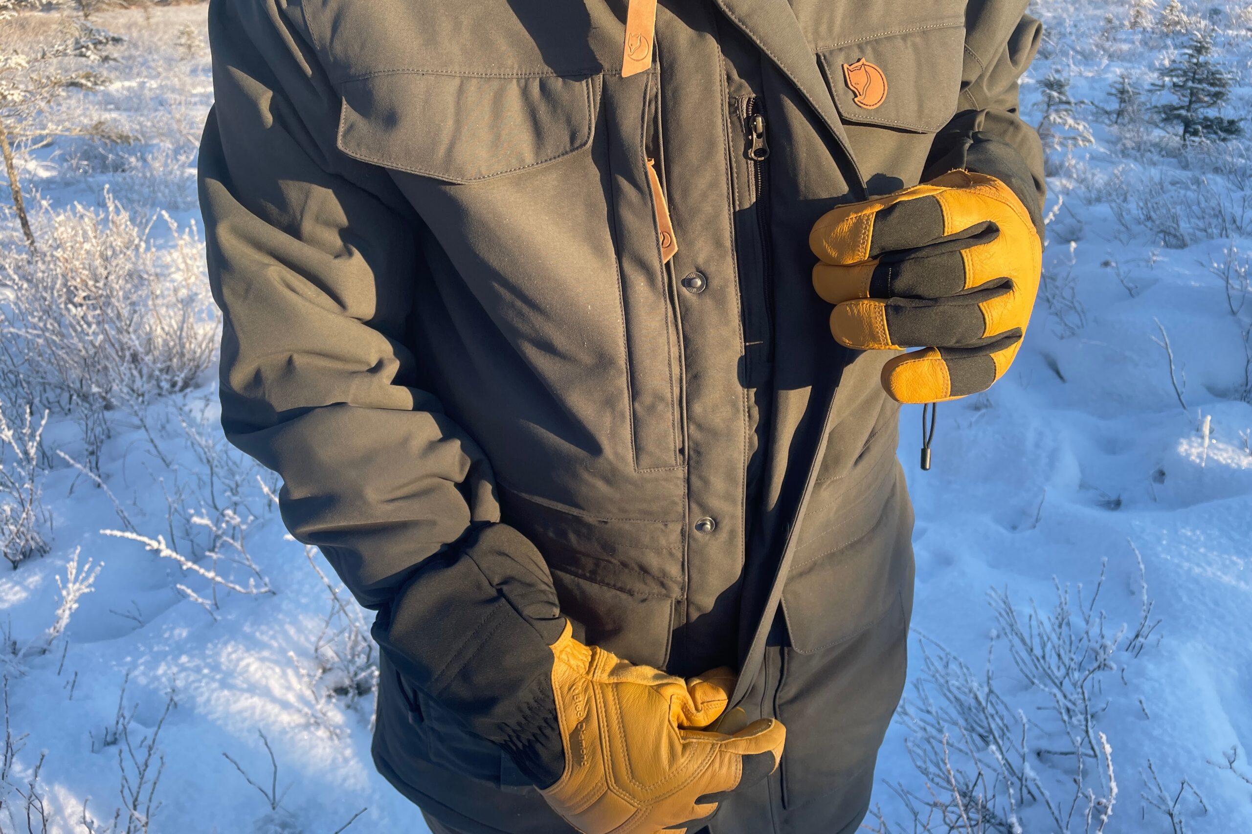 A man unzips his jacket while wearing gloves