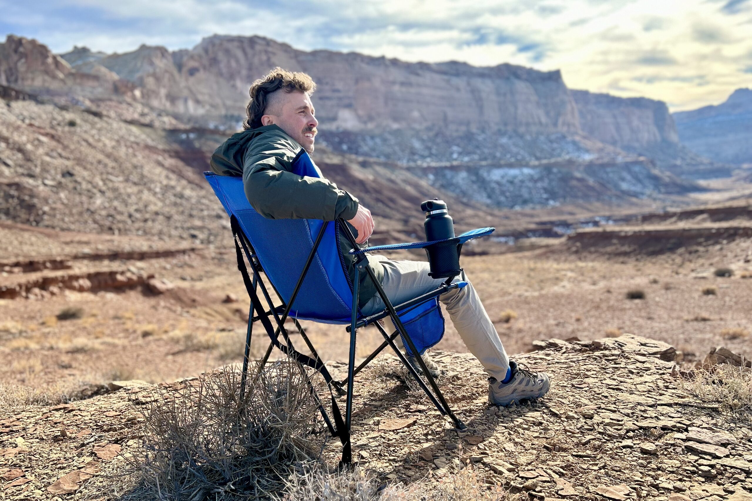 A man sits in a camping chair in a sunny desert setting.