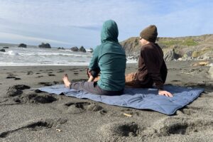 2 people sitting on the Yeti Lowlands Blanket at the beach.