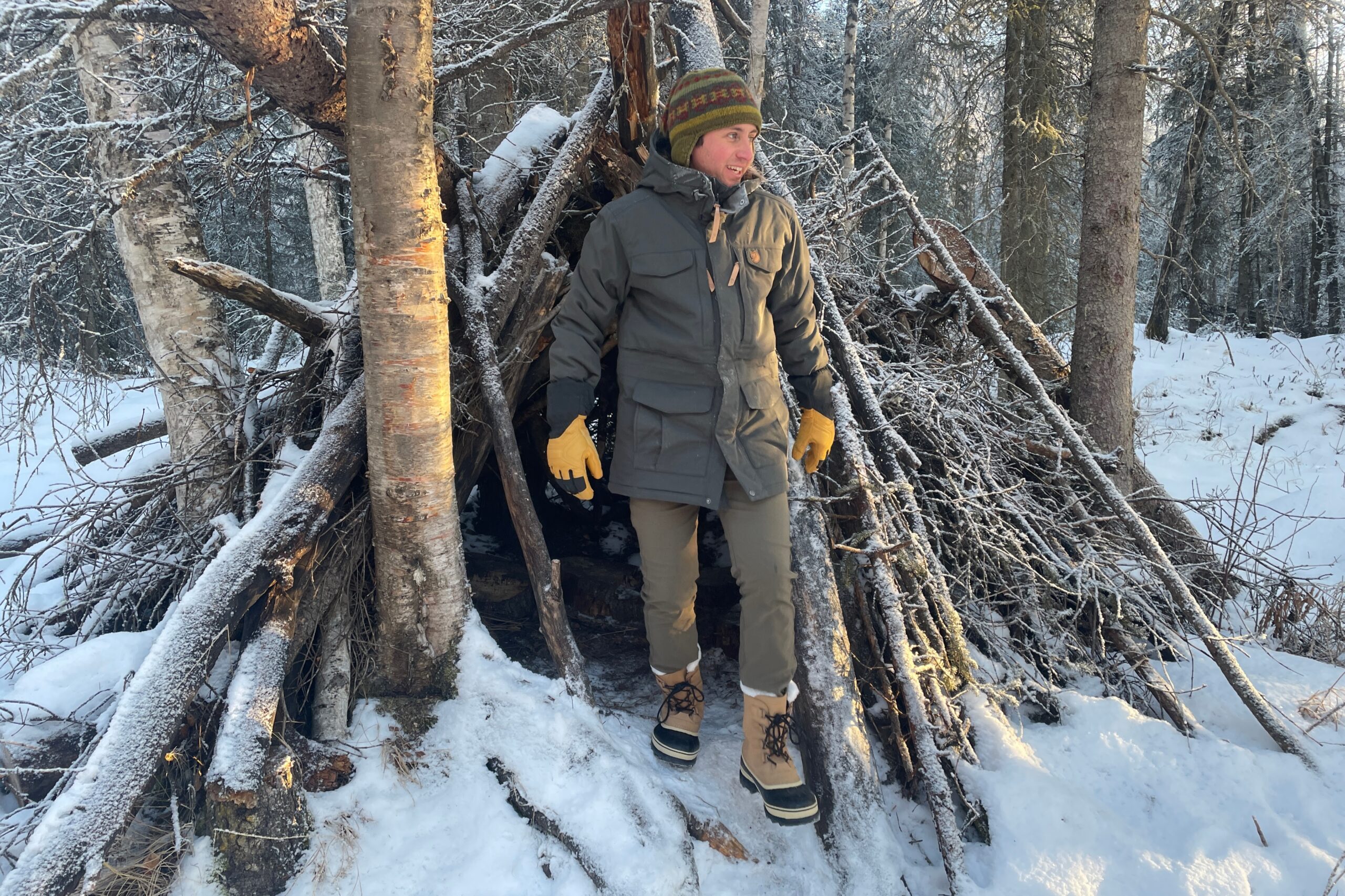 A man steps out of a shelter made of sticks.