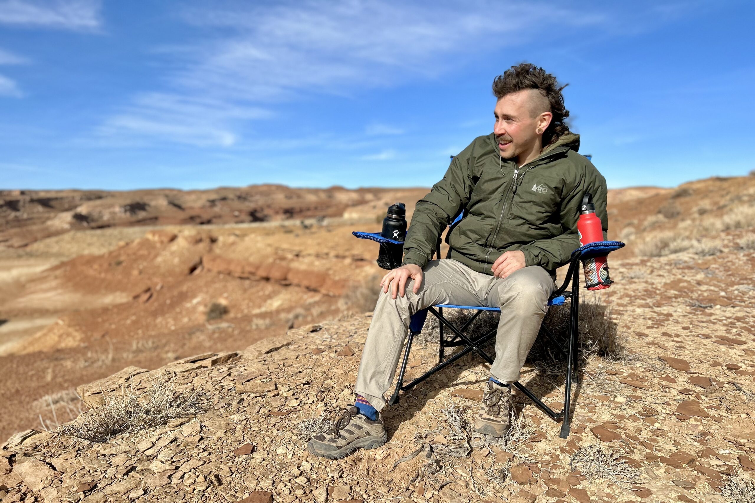 A man sits in a camping chair in a sunny desert setting.