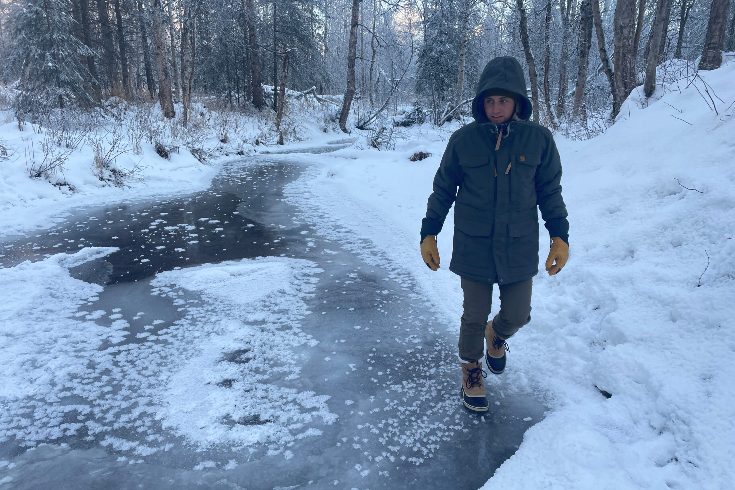 A man walks along an ice covered river.