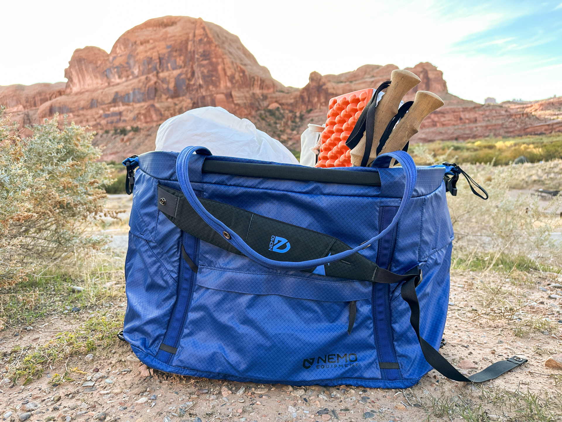 The Nemo Double Haul duffel packed with camping gear in gear hauler mode sitting on the ground in front of desert rocks.