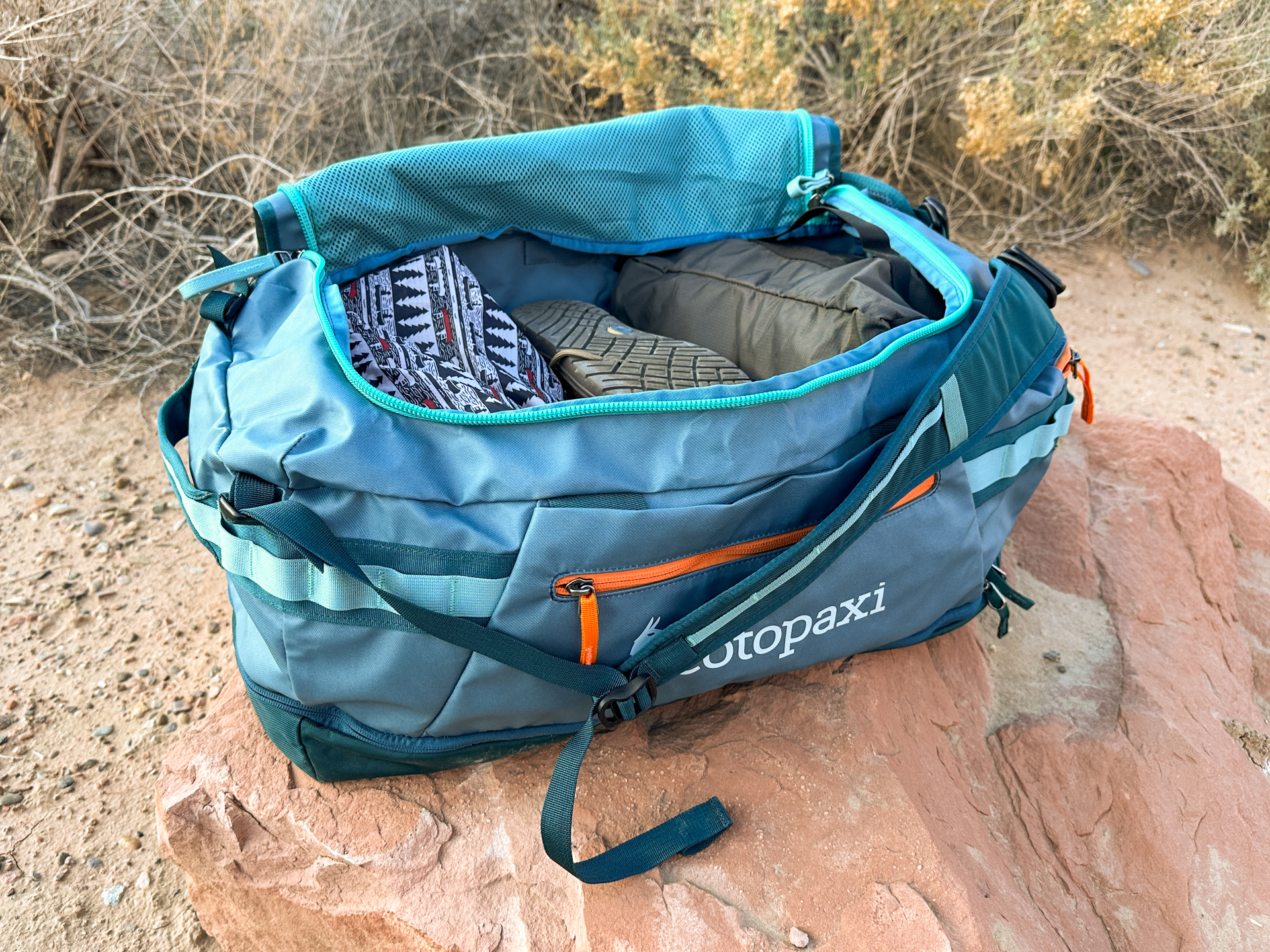 Clothing and gear stuffed into the Cotopaxi Allpa 50L, which you can see via an open lid with mesh pocket on the underside.