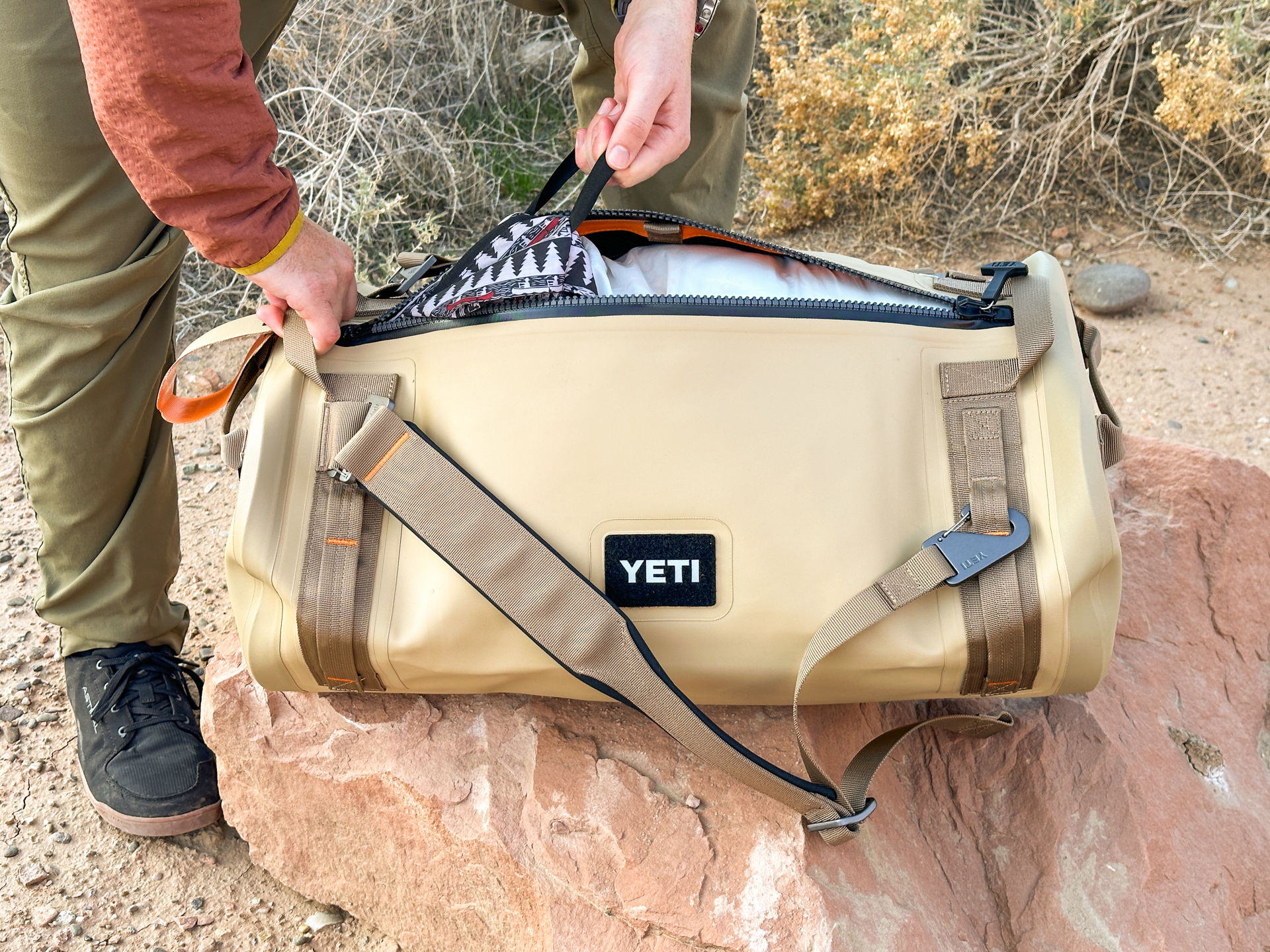 A hand pulls a stuff sack out of an unzipped Yeti Panga.