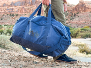 A man carries the duffel using the duffel straps.